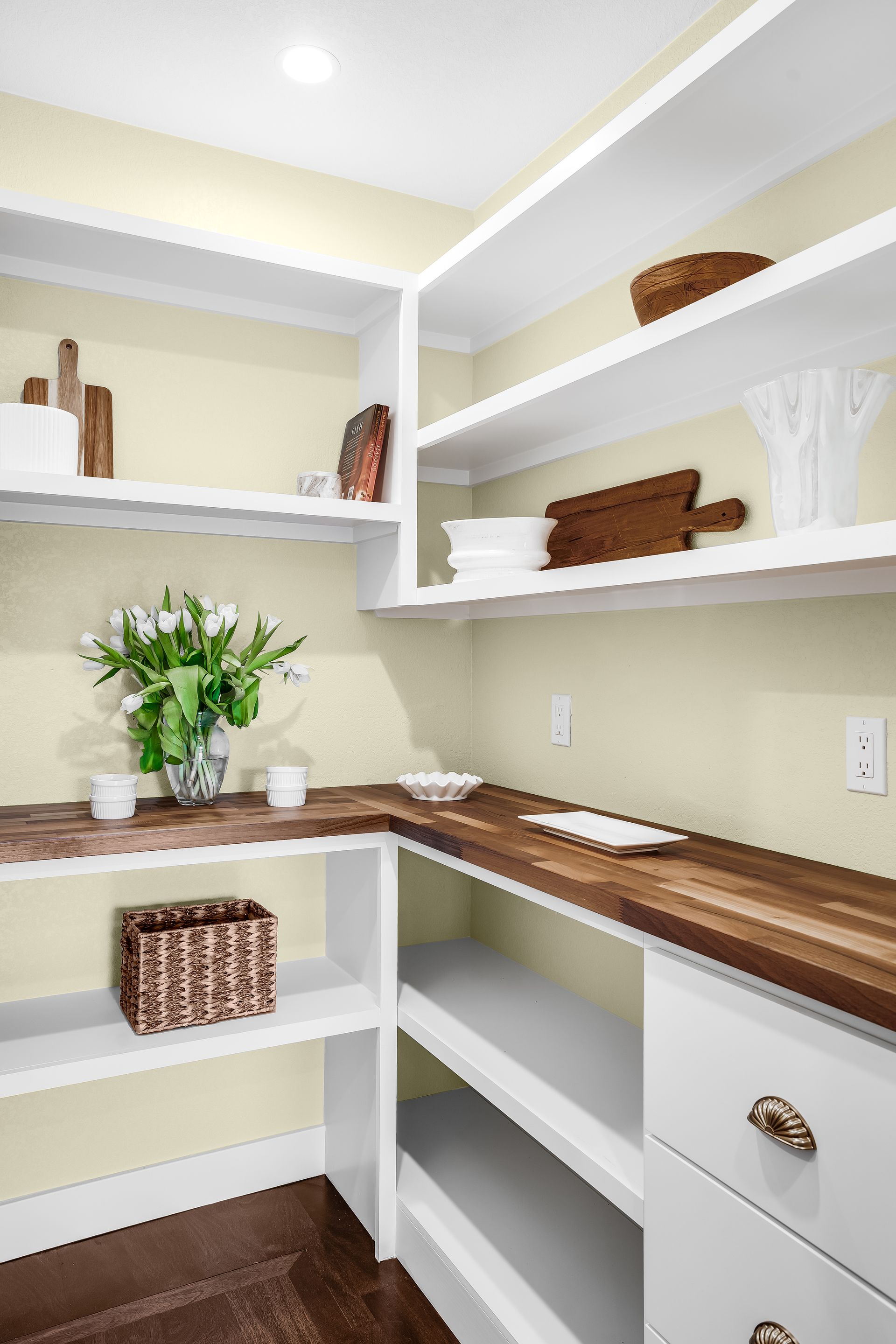 A pantry with white shelves, wooden countertops, and various decorative items.
