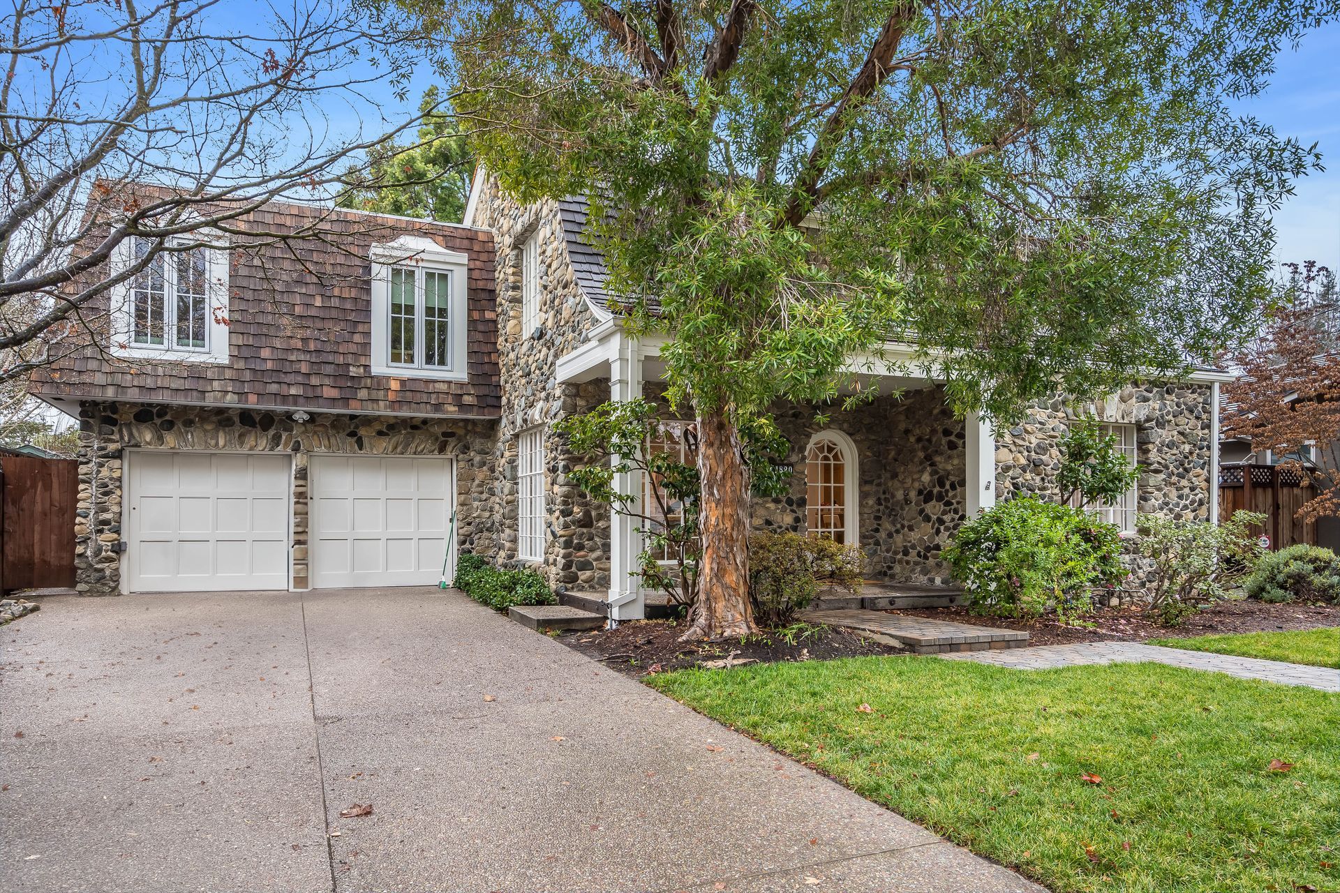 A large stone house with two garages and a tree in front of it.