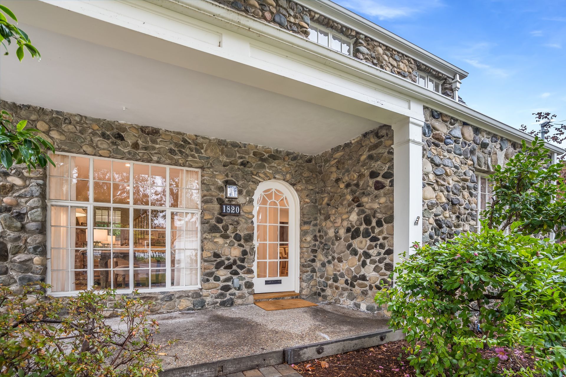 The front of a stone house with a porch and a large window.