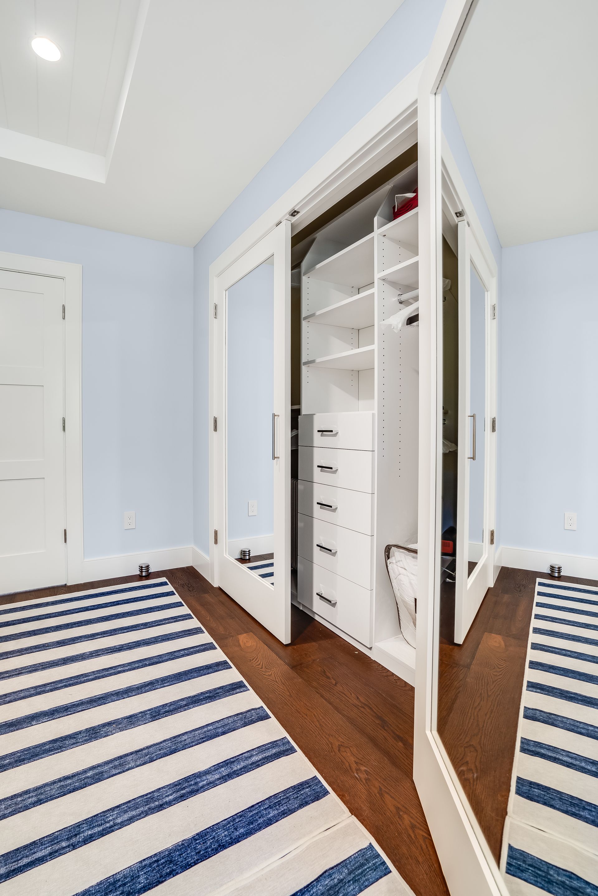 A walk in closet with a striped rug and a mirror.