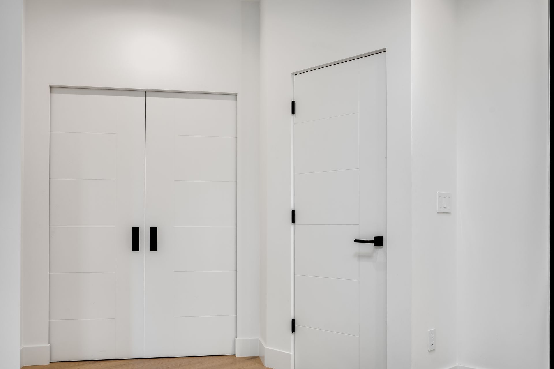 A hallway with two white doors and a black handle.