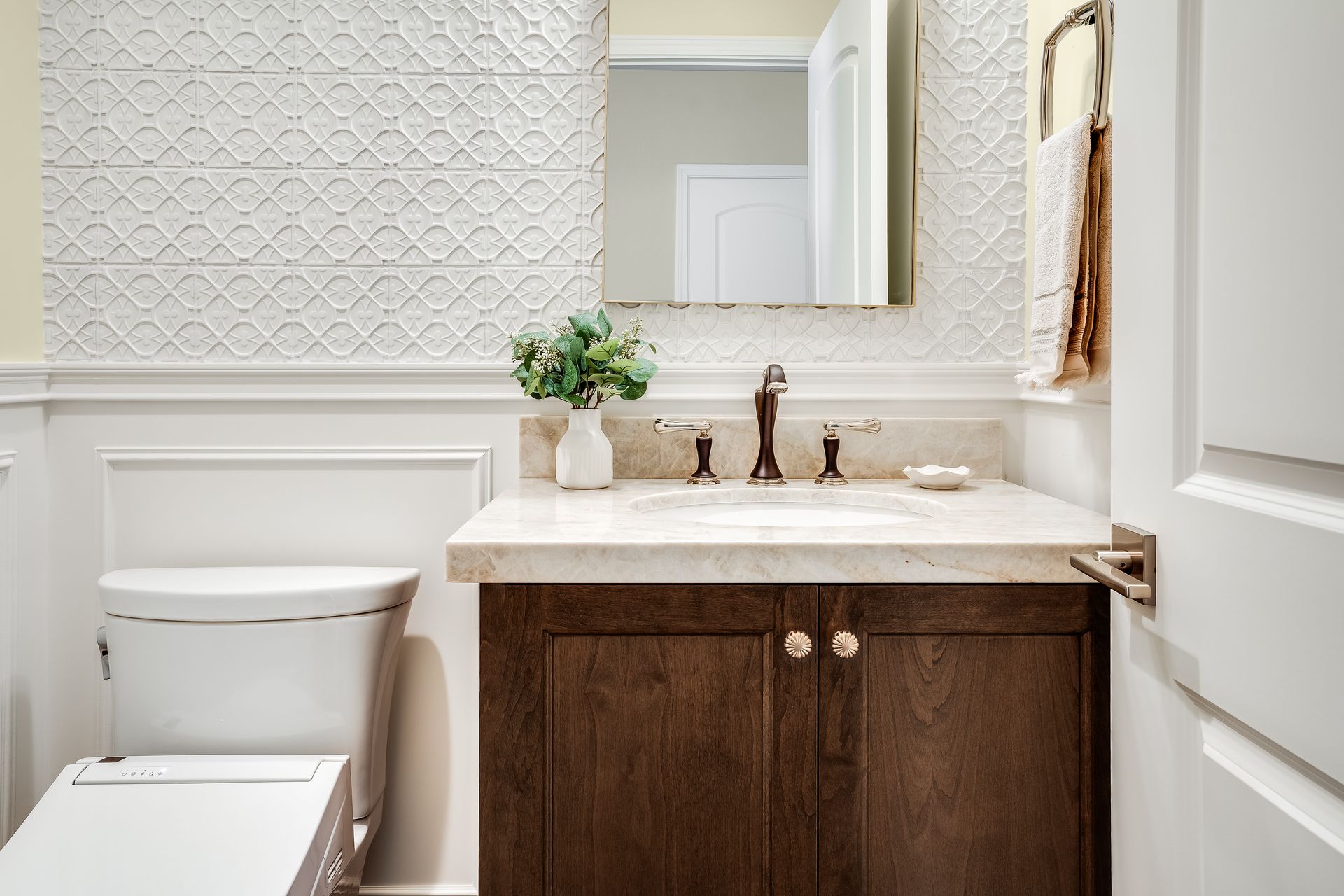 Small bathroom with wood vanity, white toilet, and patterned wall.