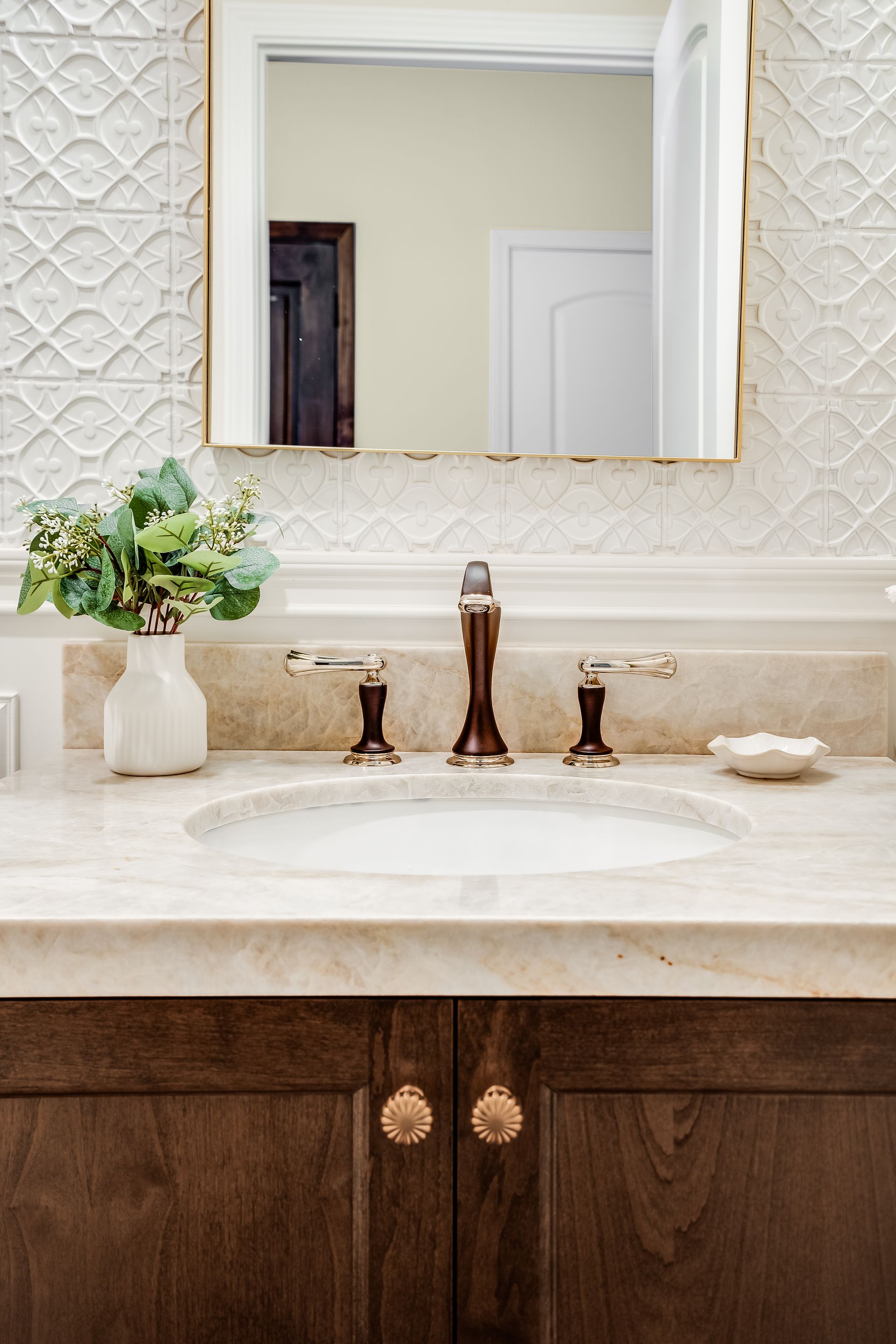Bathroom vanity with oval sink, marble countertop, dark wood cabinets, and bronze faucet. Decorative tile backsplash.