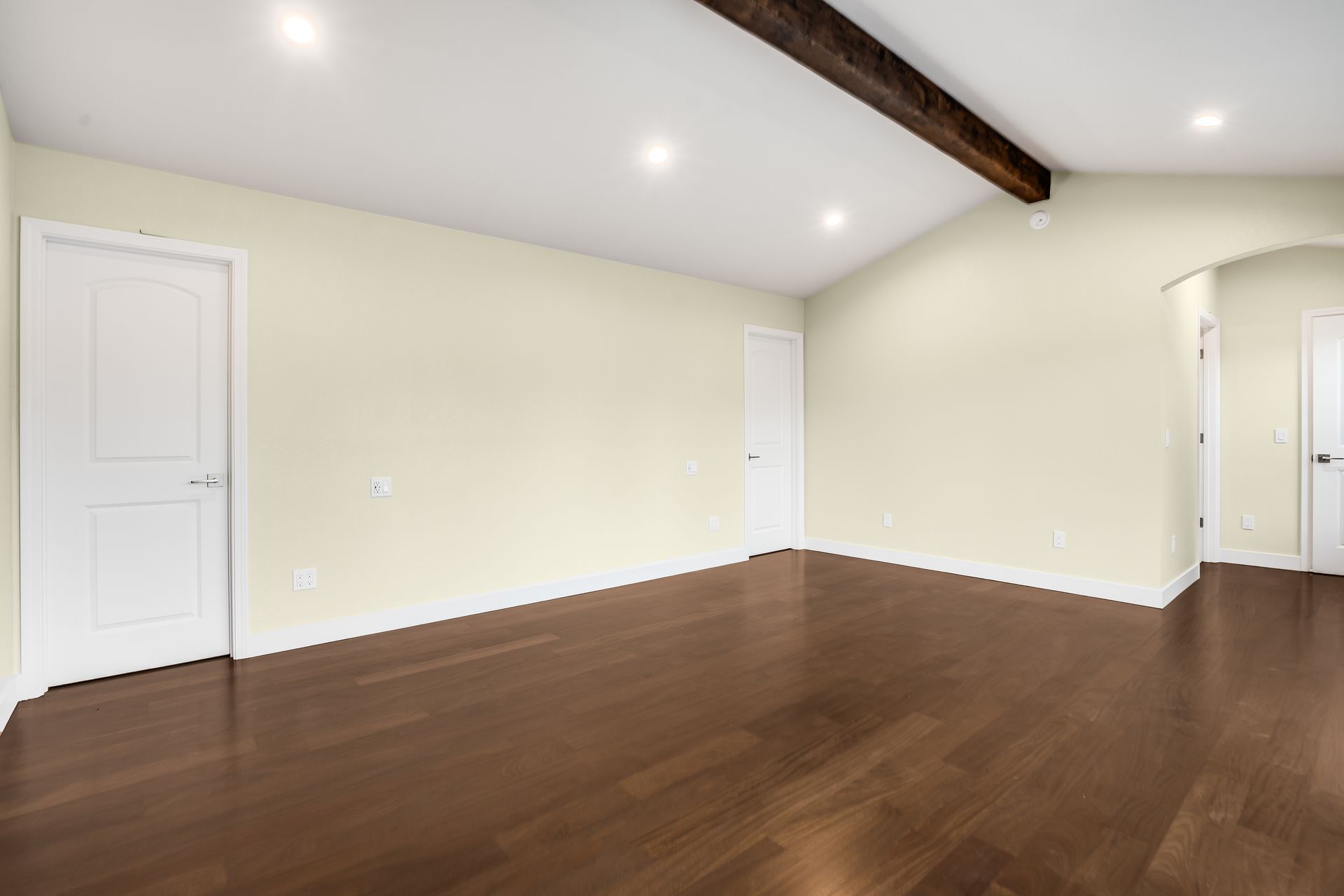 Empty room with hardwood floors, light yellow walls, white doors, and a dark wood beam on the ceiling.