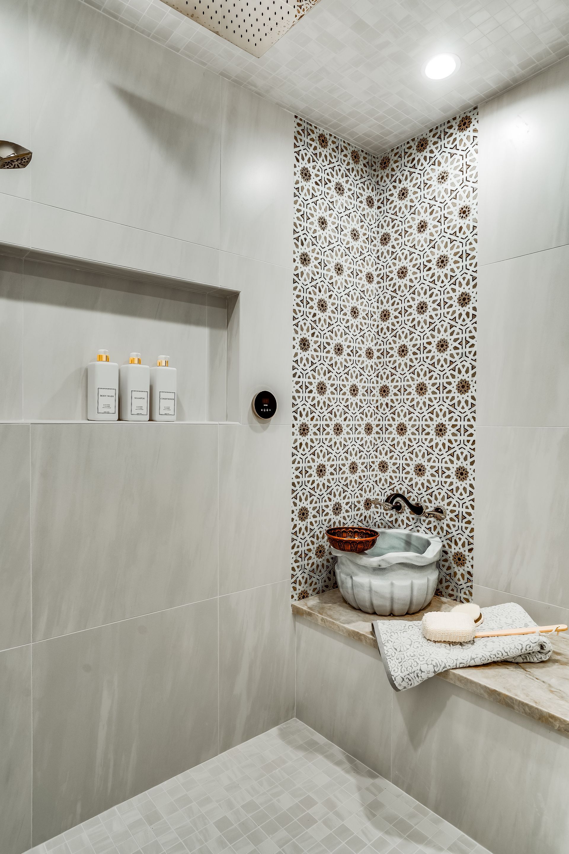 A spa-like shower with mosaic tiles, a built-in niche with toiletries, and a stone basin in a neutral color scheme.