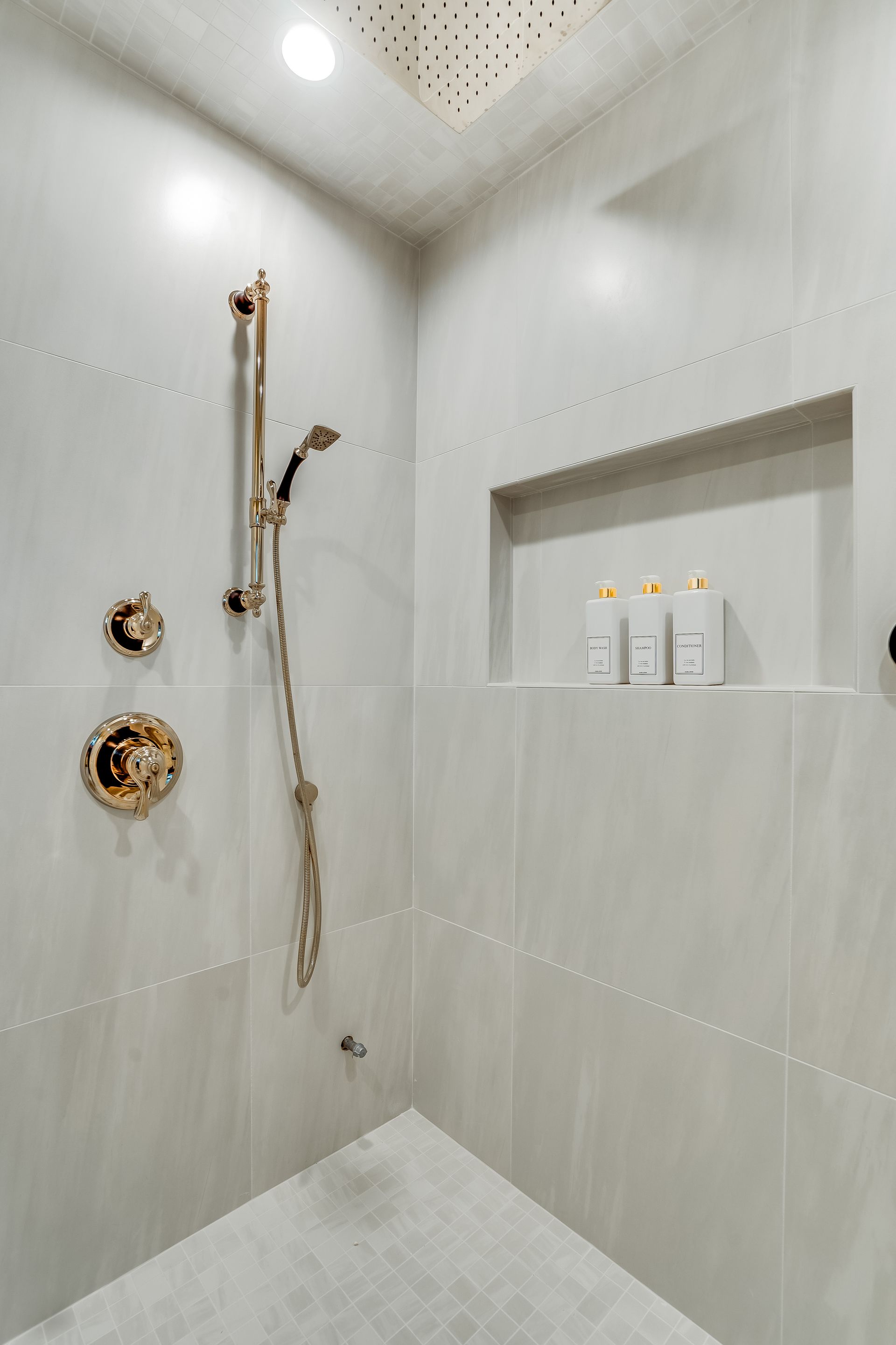 A luxurious, gray-tiled shower with gold fixtures. A built-in shelf holds toiletries.