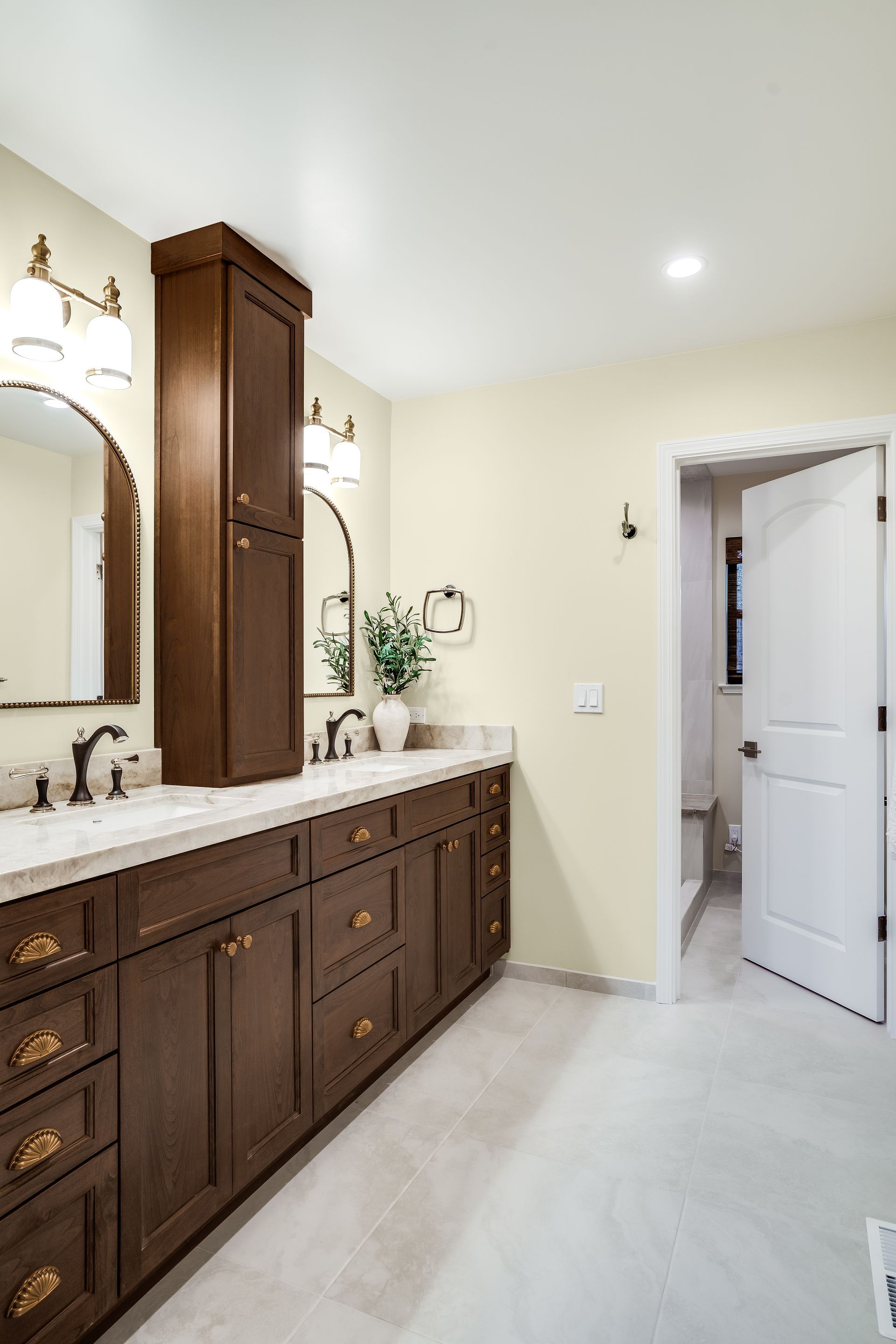 Bathroom with dark wood cabinets, light countertops, arched mirrors, and an open door to a toilet room.