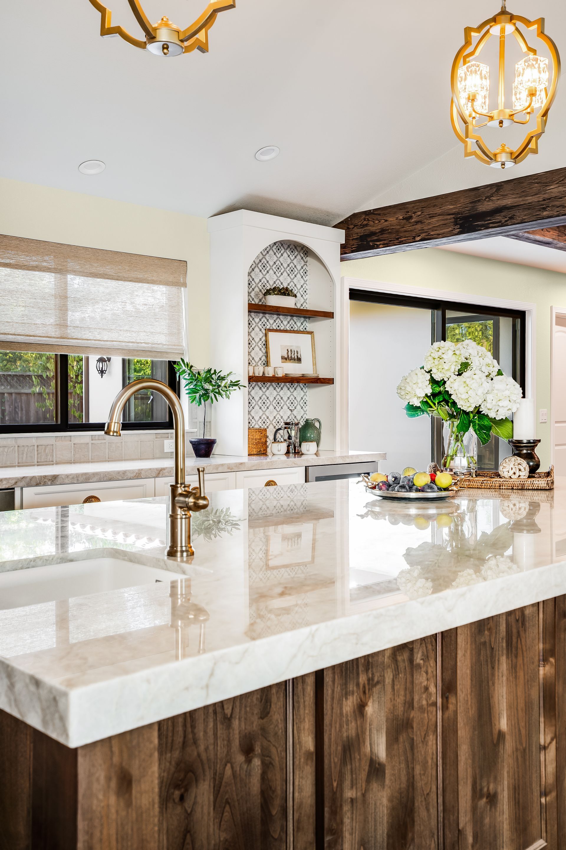 Kitchen with a marble countertop island and rustic wooden cabinets. Gold fixtures and an arched shelf.