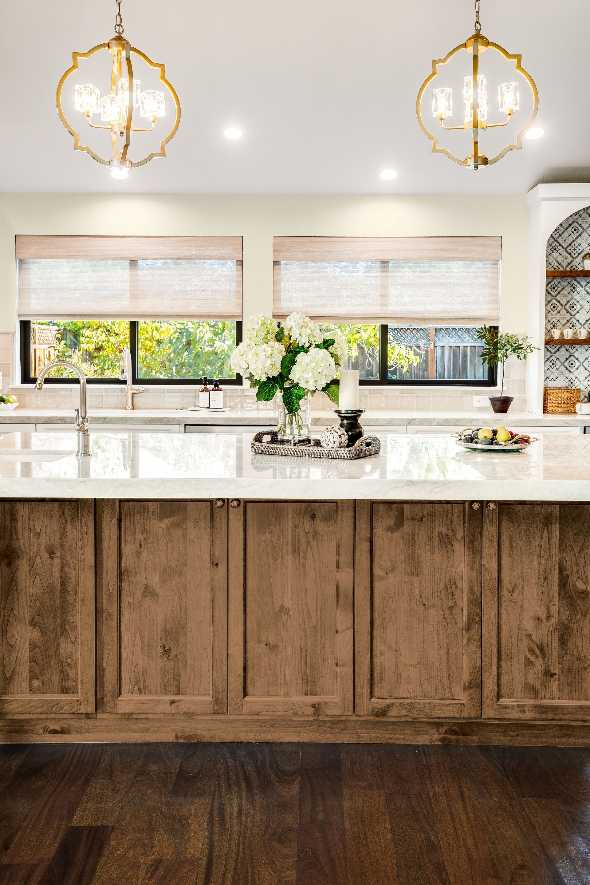Kitchen with wood cabinets, marble countertop, and gold light fixtures.
