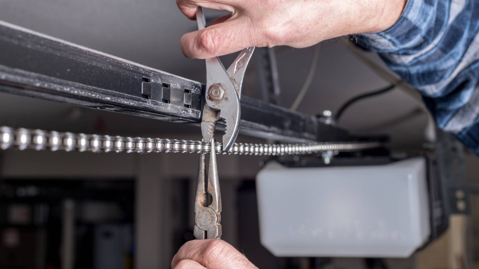 Two-car garage with tan doors, attached to a two-story beige house under a bright blue sky.