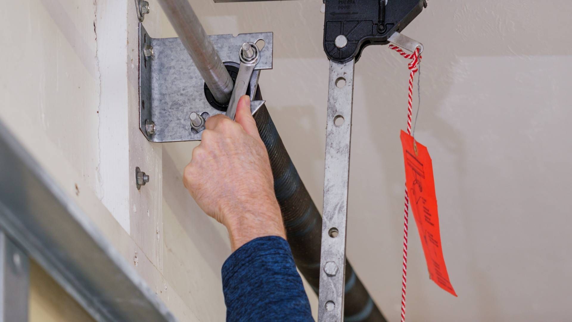 Two-car garage with tan doors, attached to a two-story beige house under a bright blue sky.