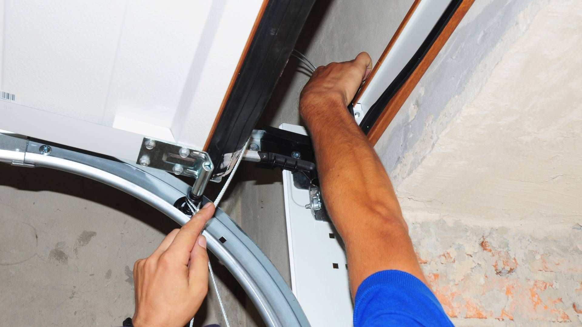 Person in blue shirt repairing a garage door track with a screwdriver.