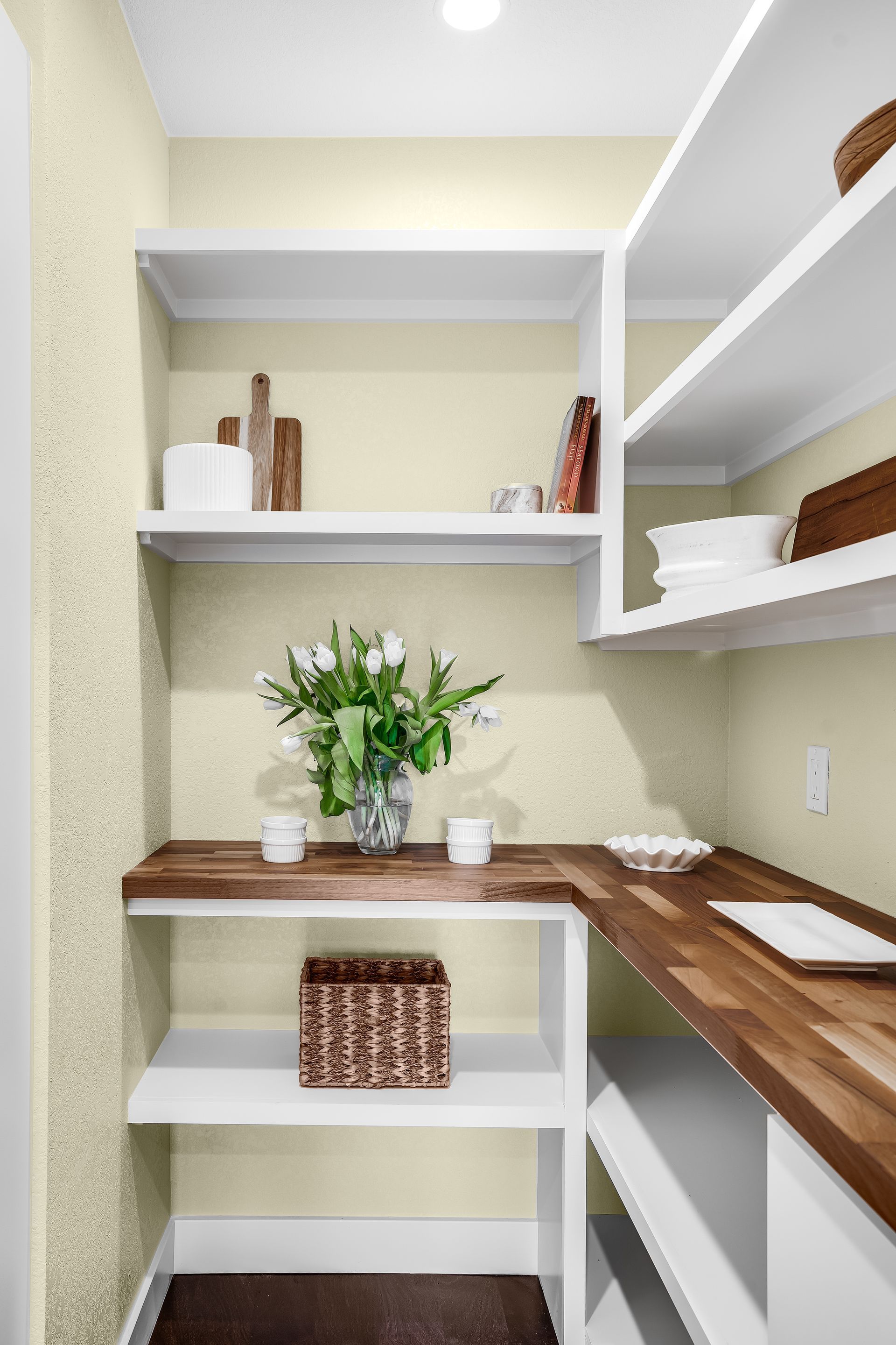 Small pantry with white shelves, wood countertops, and yellow walls holding items.