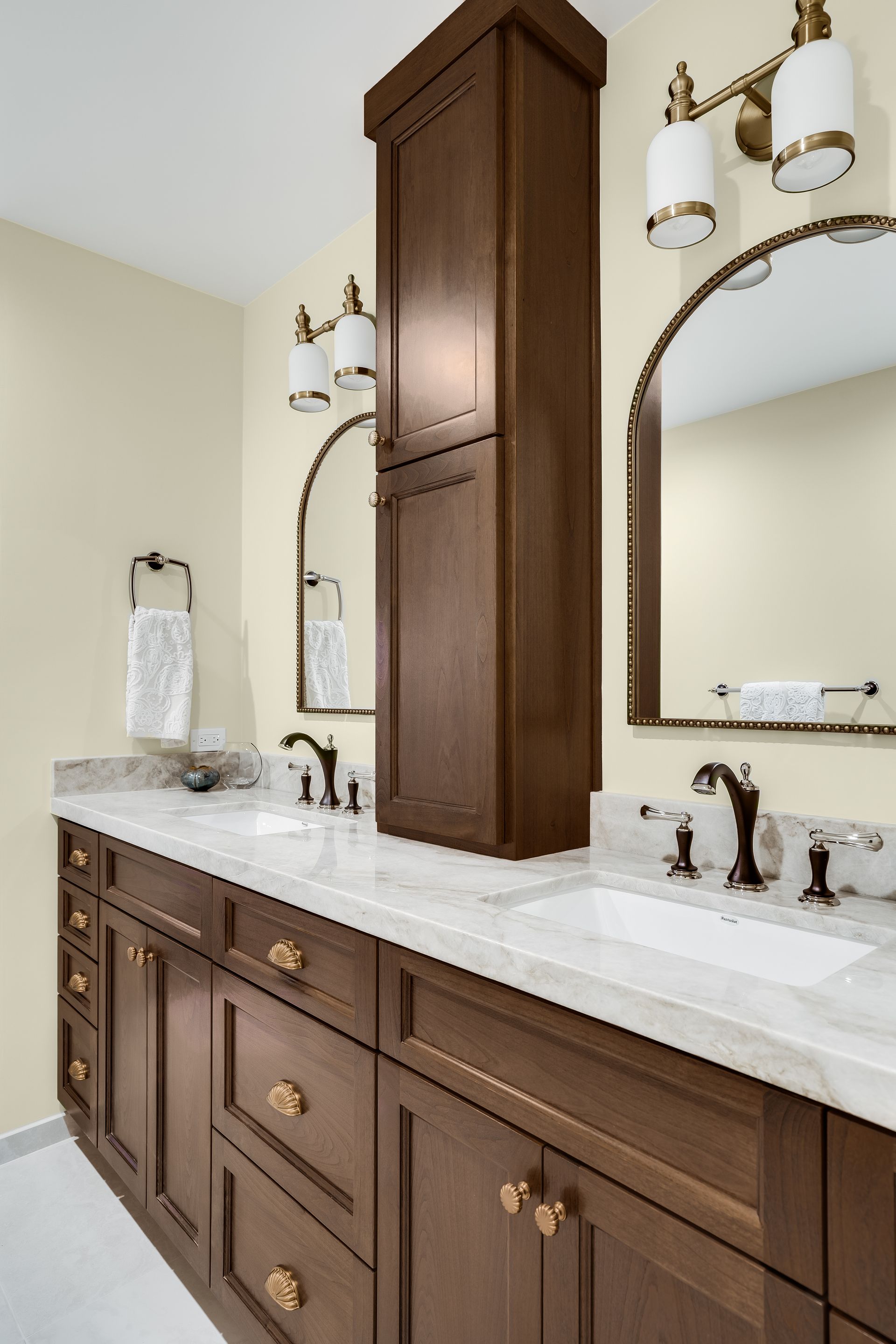 Bathroom with a double vanity, dark wood cabinets, marble countertop, and gold fixtures.