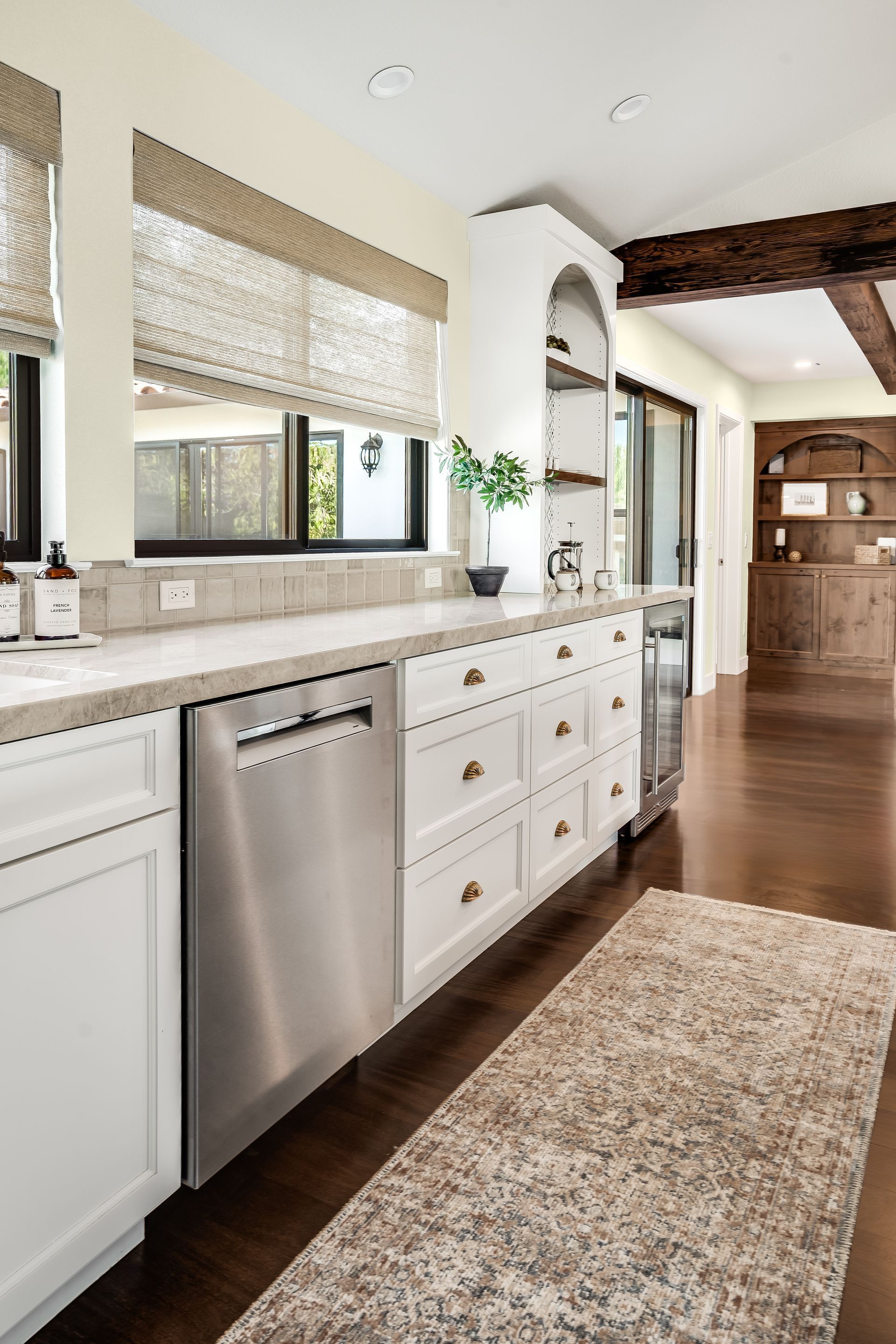 Modern white kitchen with stainless steel dishwasher, patterned rug, and wood floors.