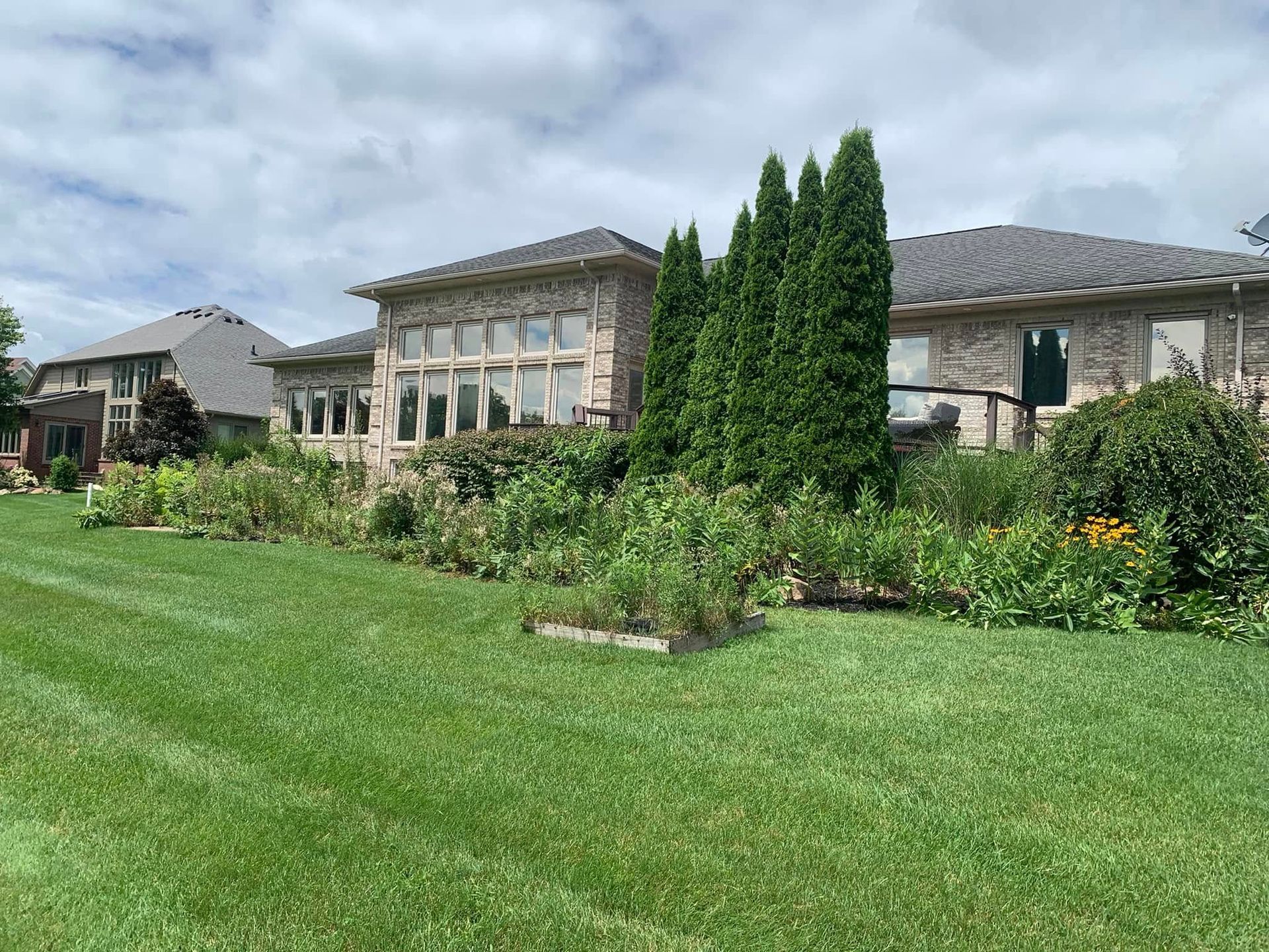 Backyard with brick house, garden beds, and green lawn under a cloudy sky.