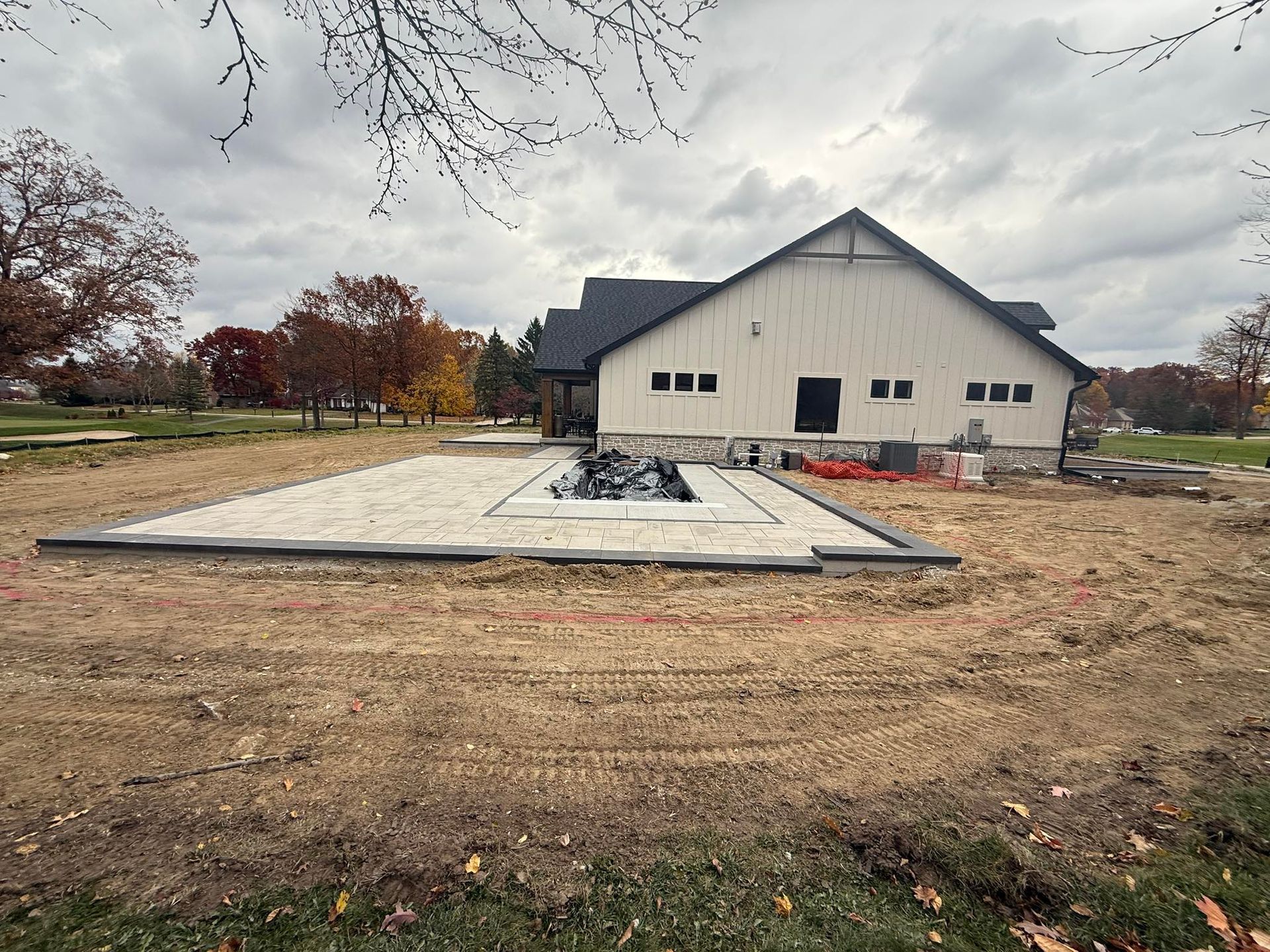 Construction of a patio with fire pit next to a light-colored building under a cloudy sky.