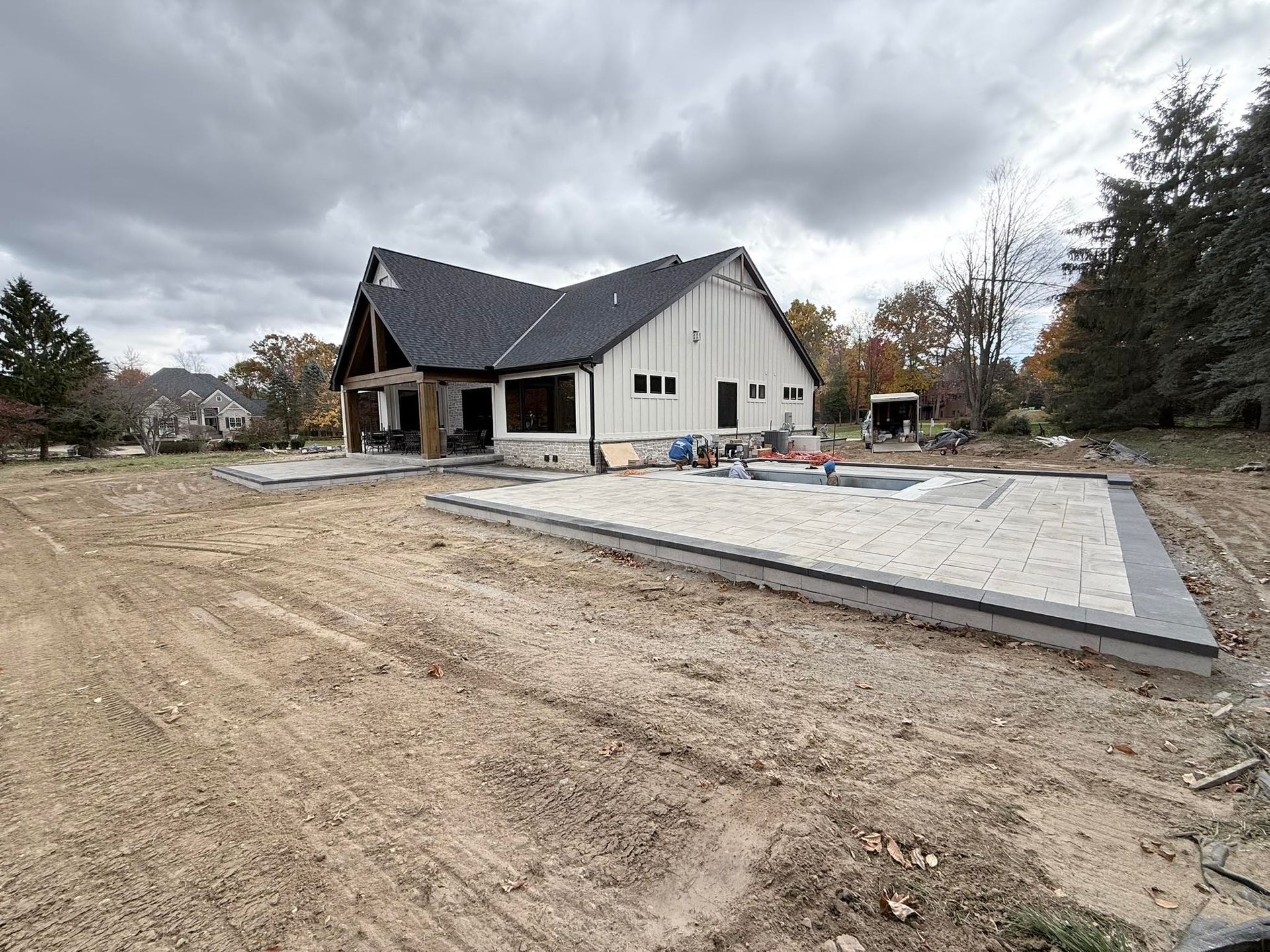 House under construction with a black roof, white siding, and a pool foundation. Overcast sky.