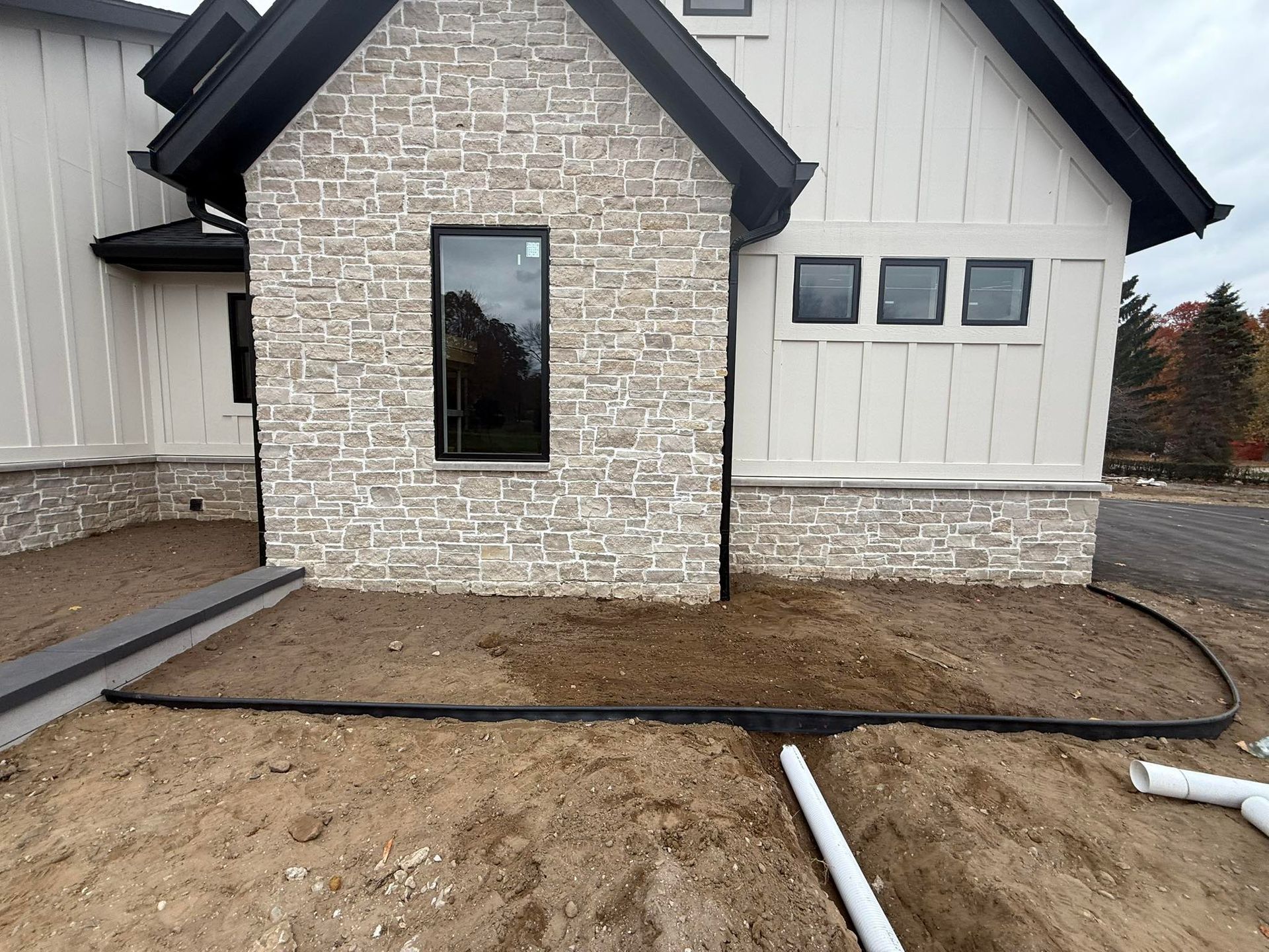 Exterior of a modern house, showing stone and siding. Black trim, dark windows, and unfinished landscaping.