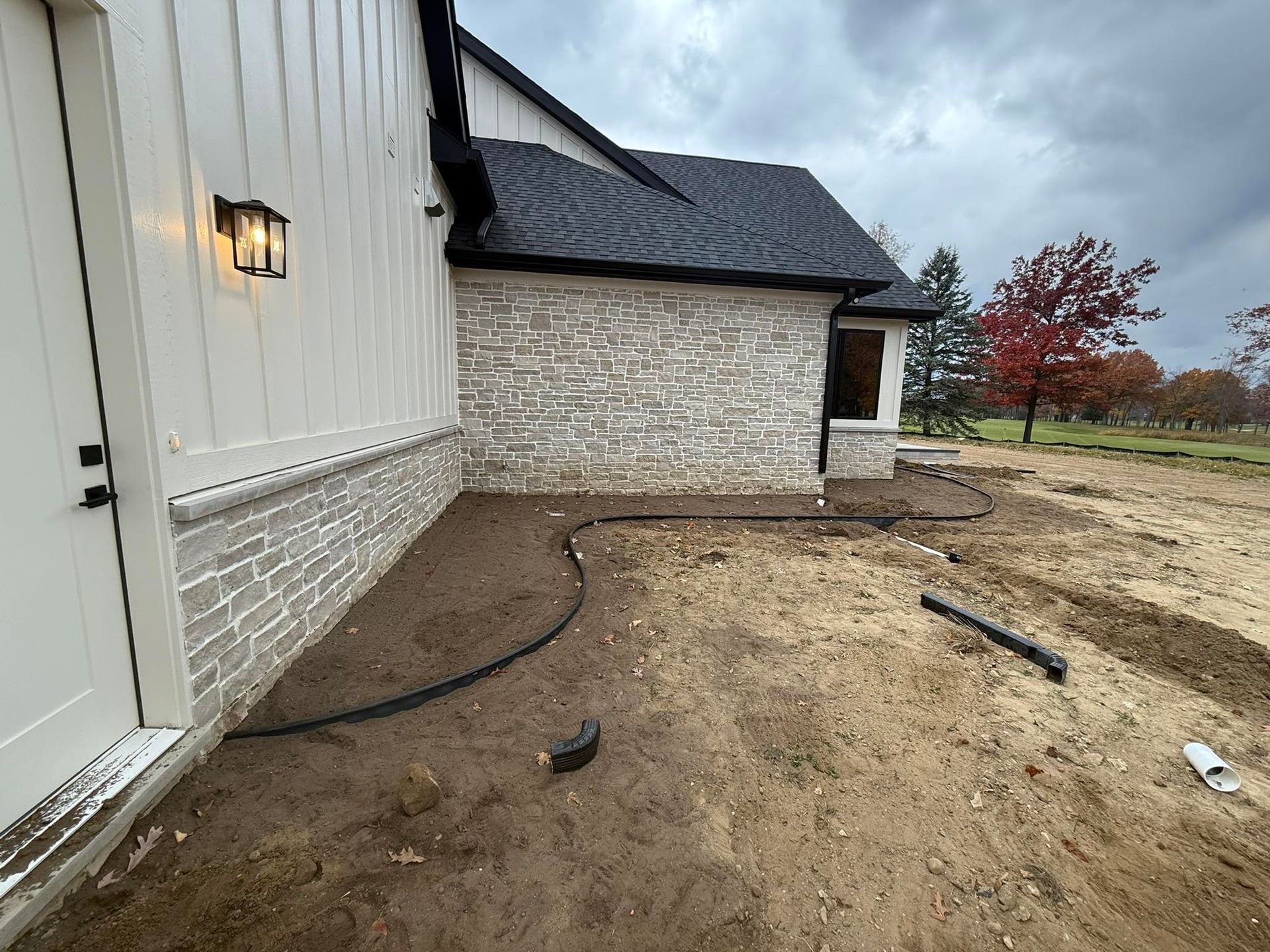 Exterior of a house with stone and white siding, unfinished landscaping, and a black gutter.