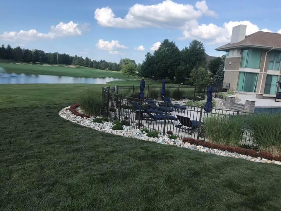 Lush green lawn with a lake view, patio with black umbrellas and a modern house under a bright blue sky.