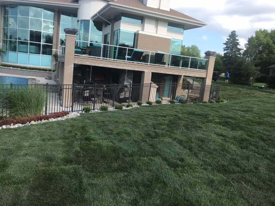 Lush green lawn slopes up to a modern home with glass balconies. A fence borders the yard.