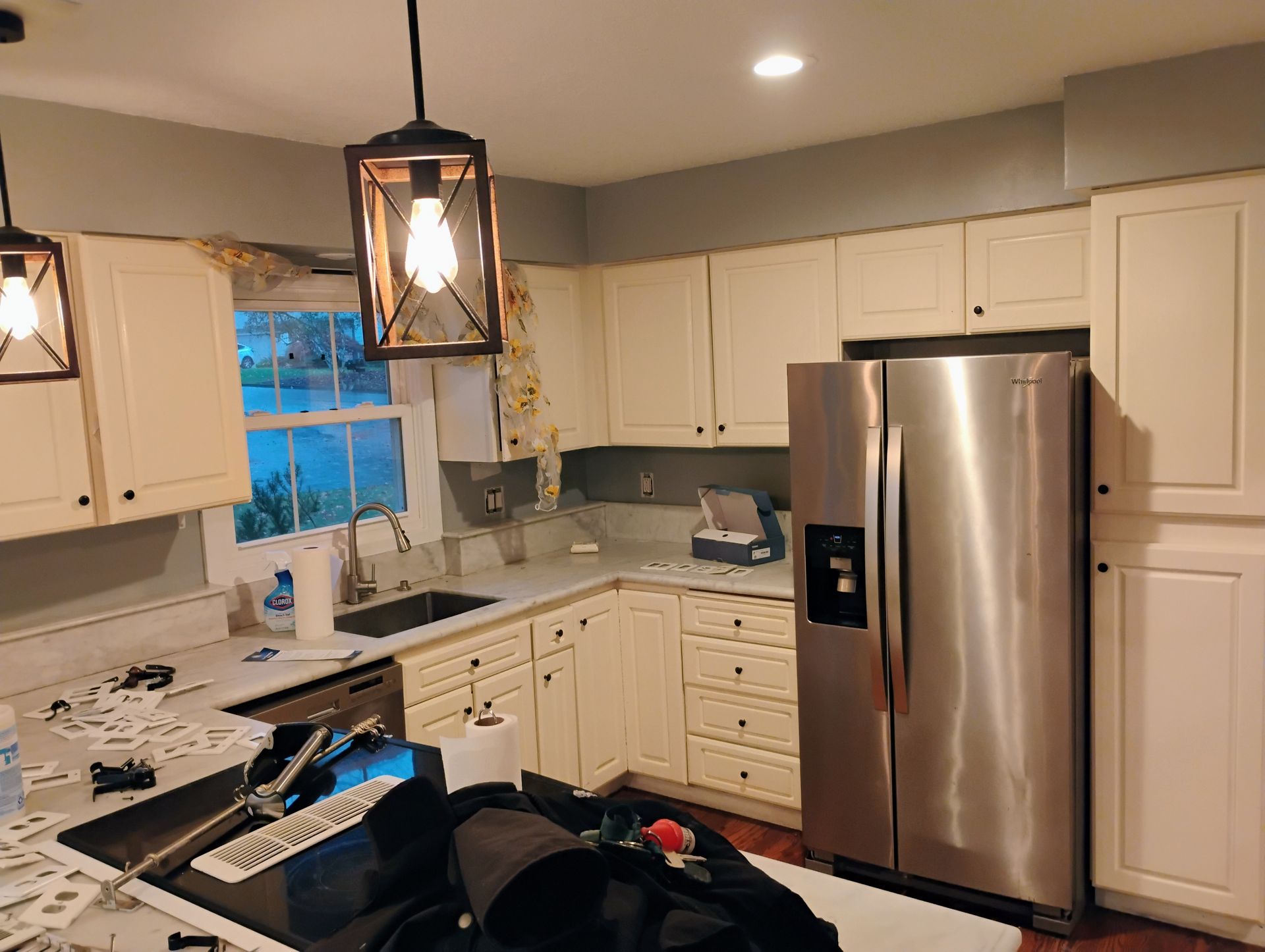 Kitchen with off-white cabinets, stainless steel refrigerator, and hanging lights. Sink and countertops visible.
