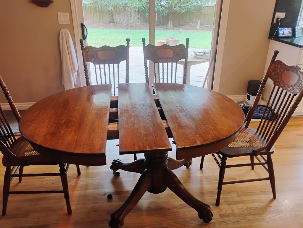Dining table with two leaves extended and four chairs. Brown wood, set near a window.
