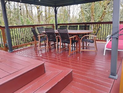 Red deck with dining table and chairs under a gazebo, surrounded by trees.
