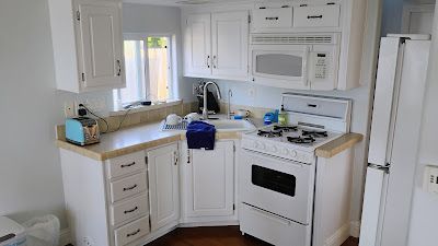 Small white kitchen with cabinets, stove, microwave, and sink.