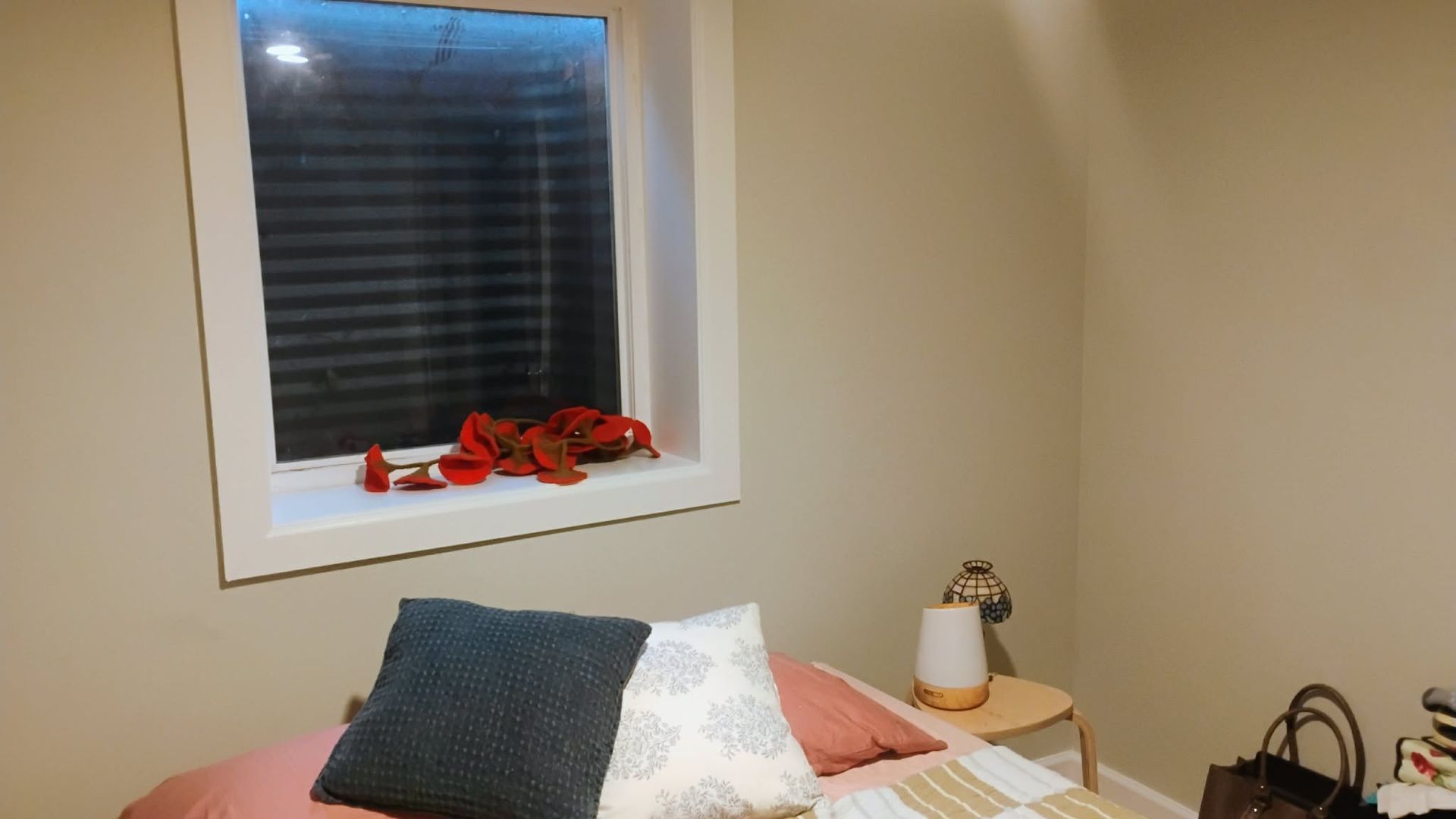 Bedroom corner with a bed, window, and small table. Pink, blue, and white pillows on the bed.