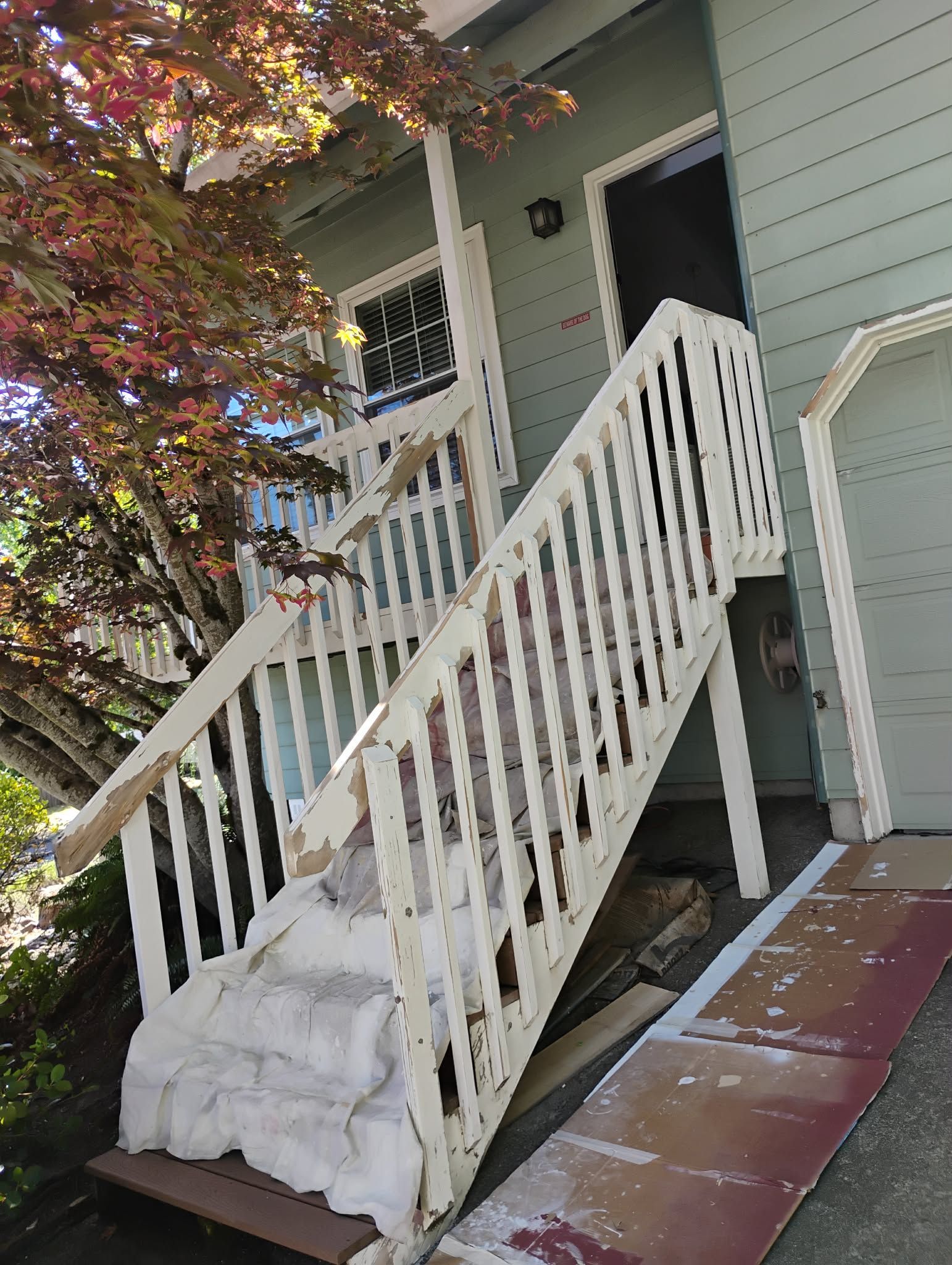 White wooden stairs leading to a light blue house entrance, with a tree on the left.