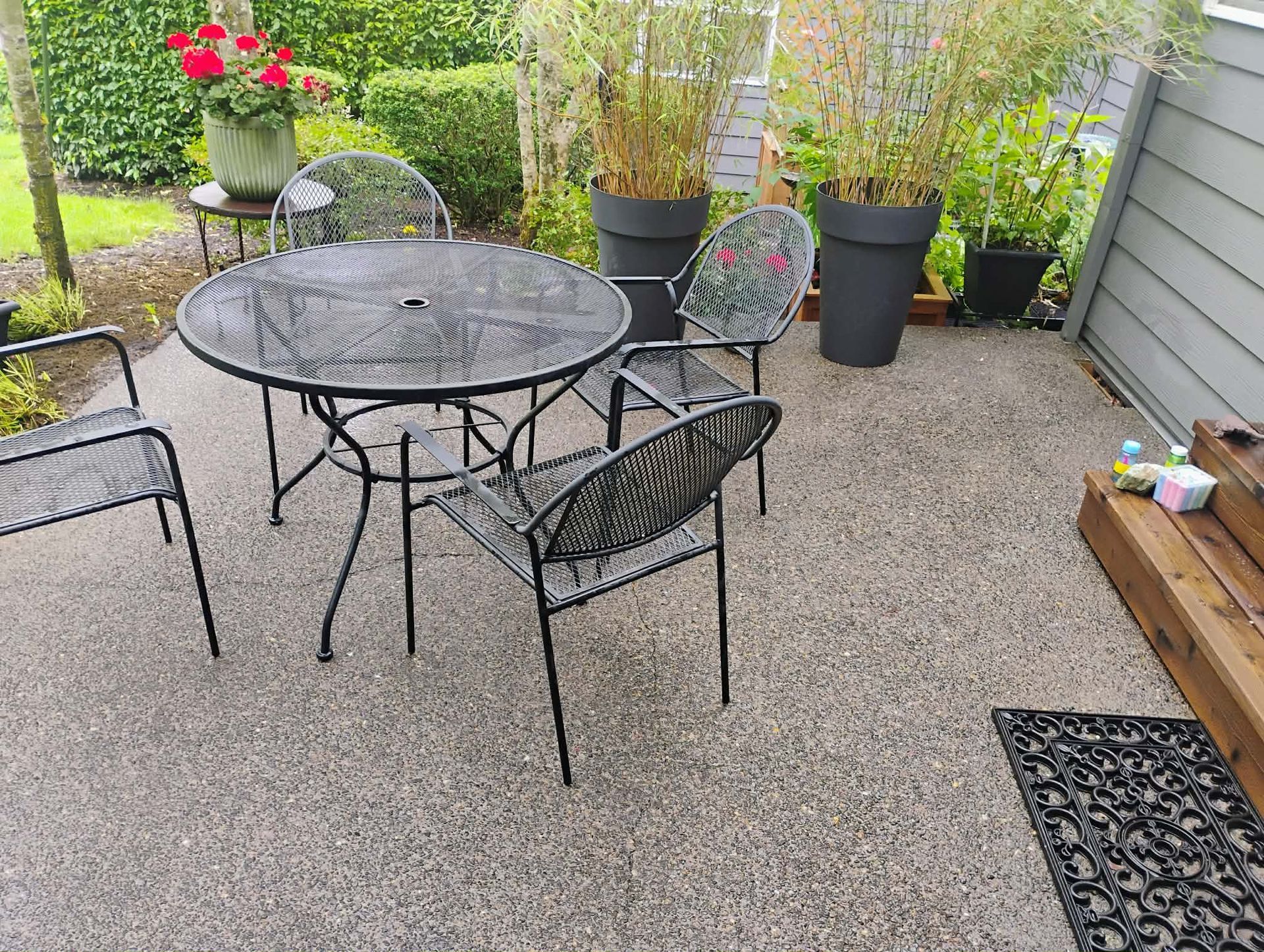 Patio with a metal table and chairs on gravel, potted plants, and a doormat.