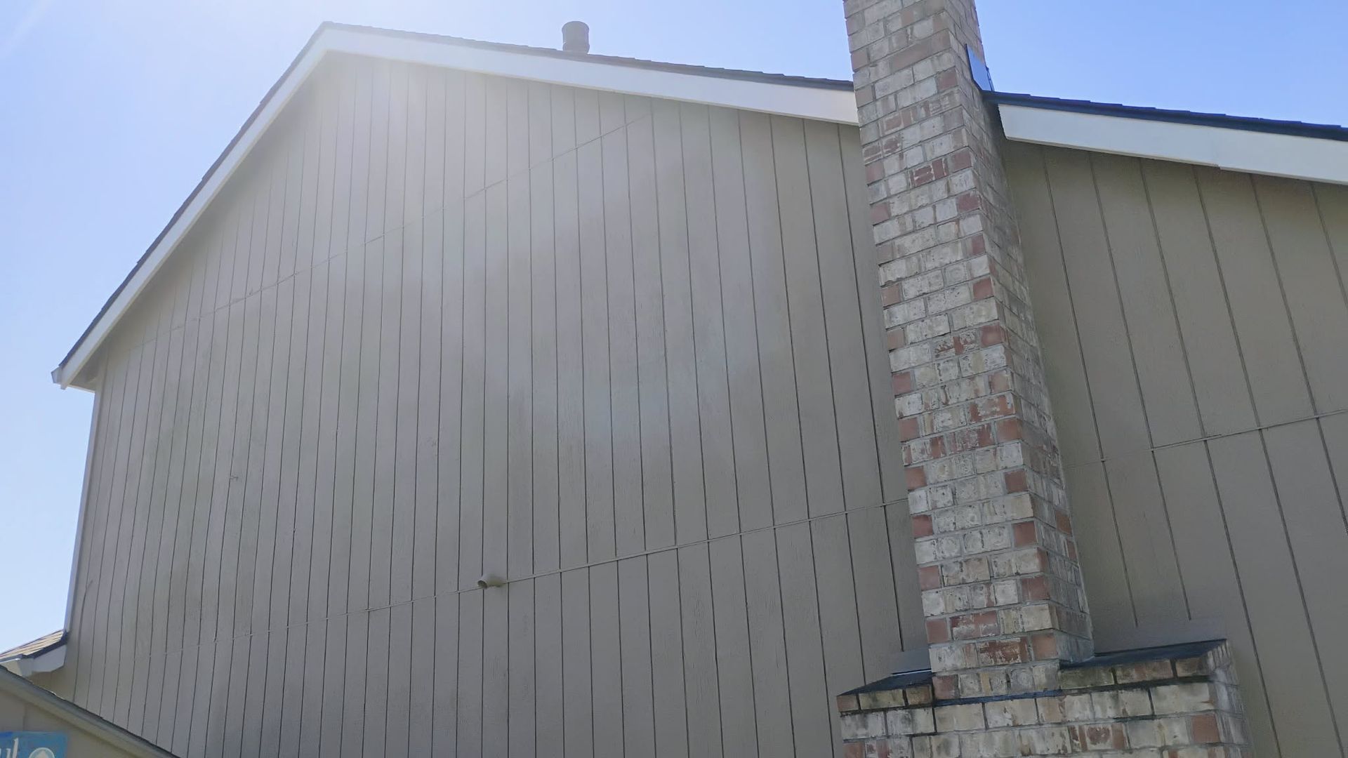 Tan house with a brick chimney against a blue sky.