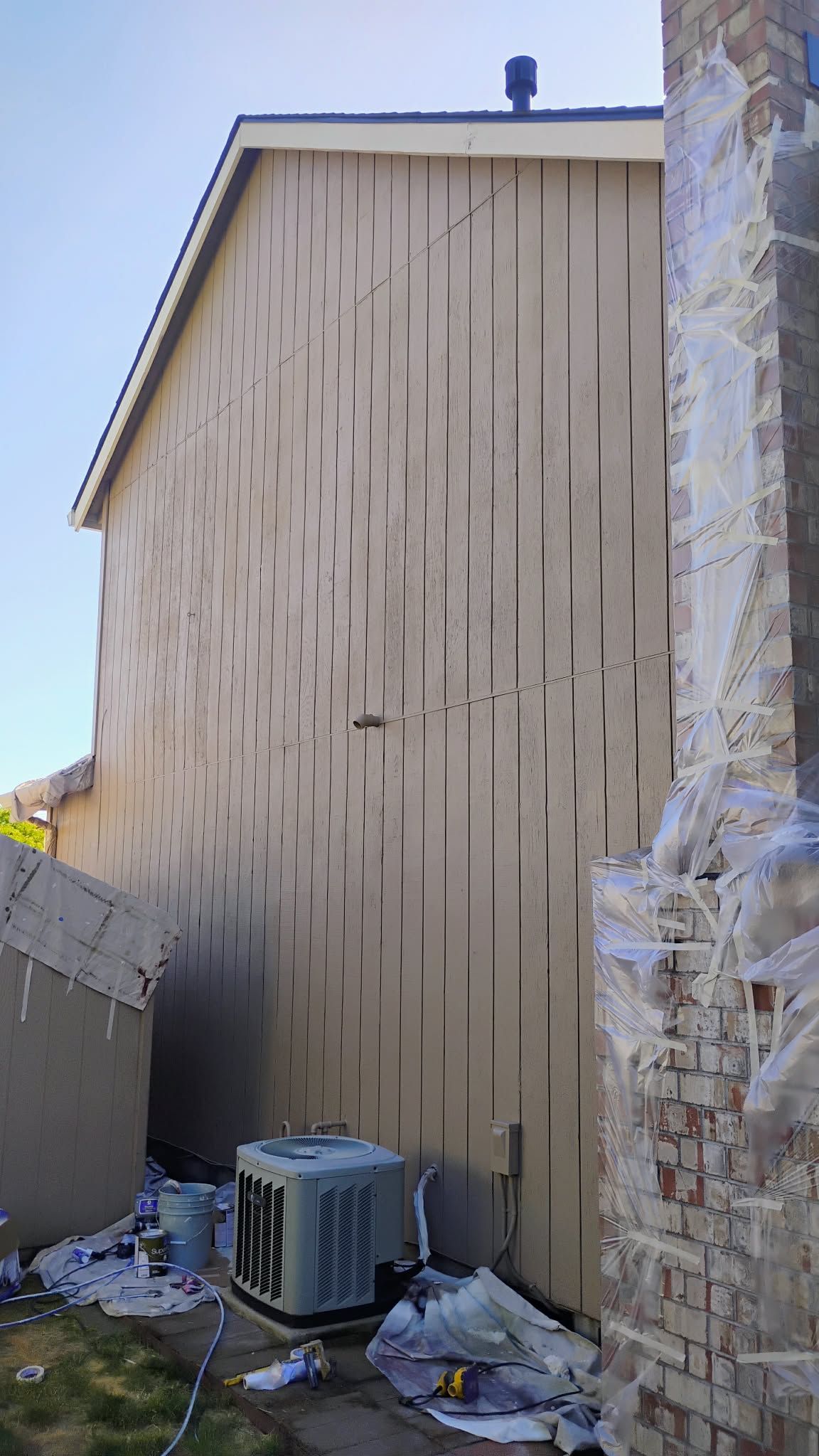 Beige siding with vertical grooves on a two-story building, next to a weathered brick chimney and an air conditioning unit.