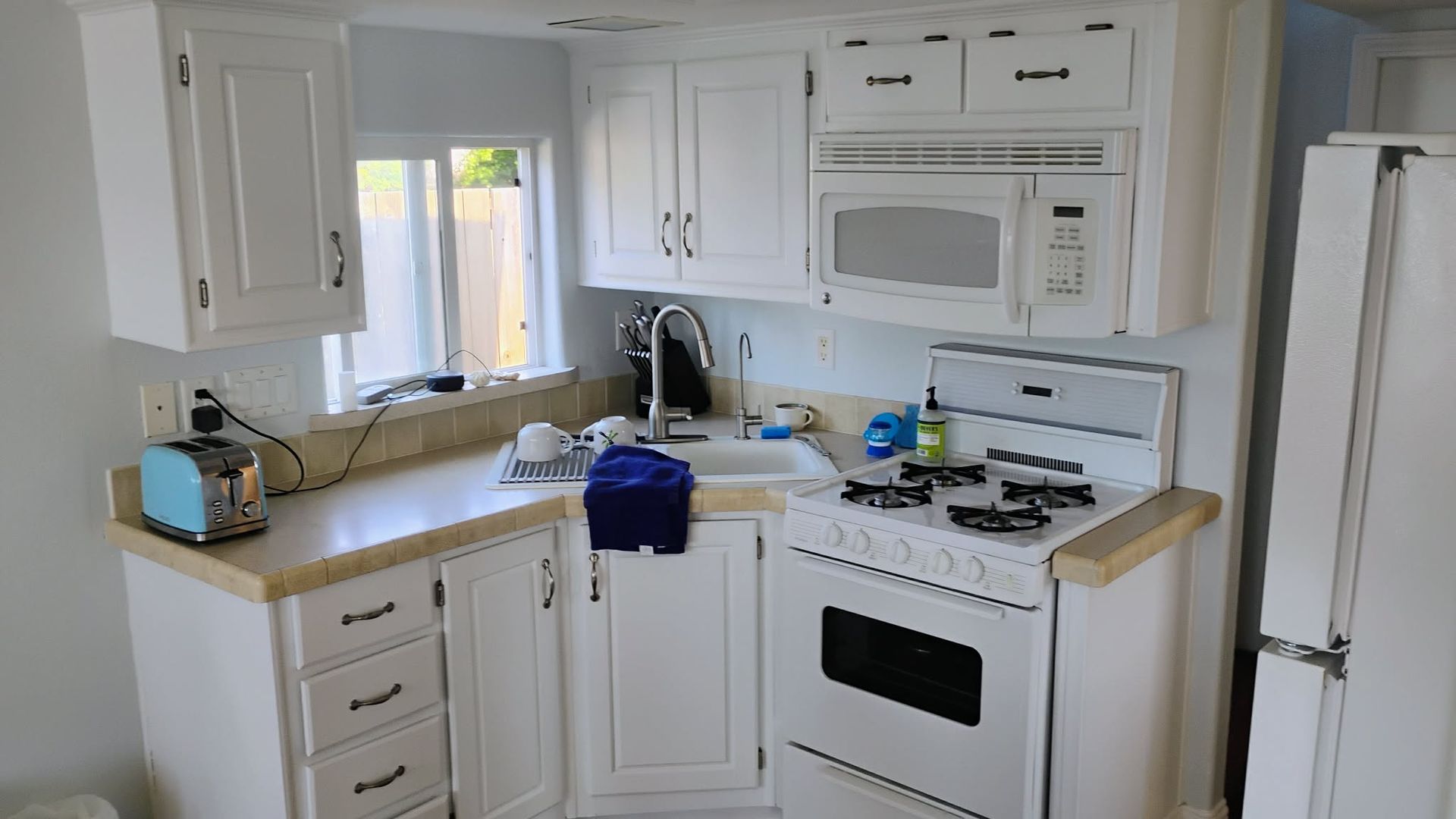 White kitchen with cabinets, microwave, sink, stove, and a blue toaster.