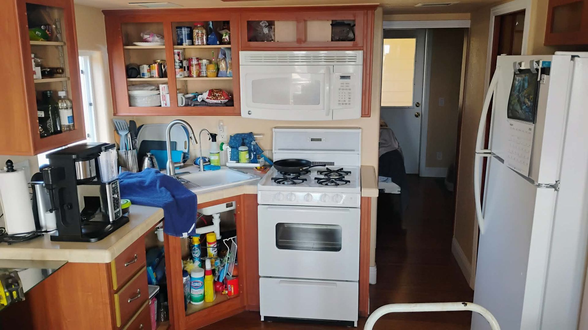 Kitchen interior with wooden cabinets, white appliances, and a hallway in the background.