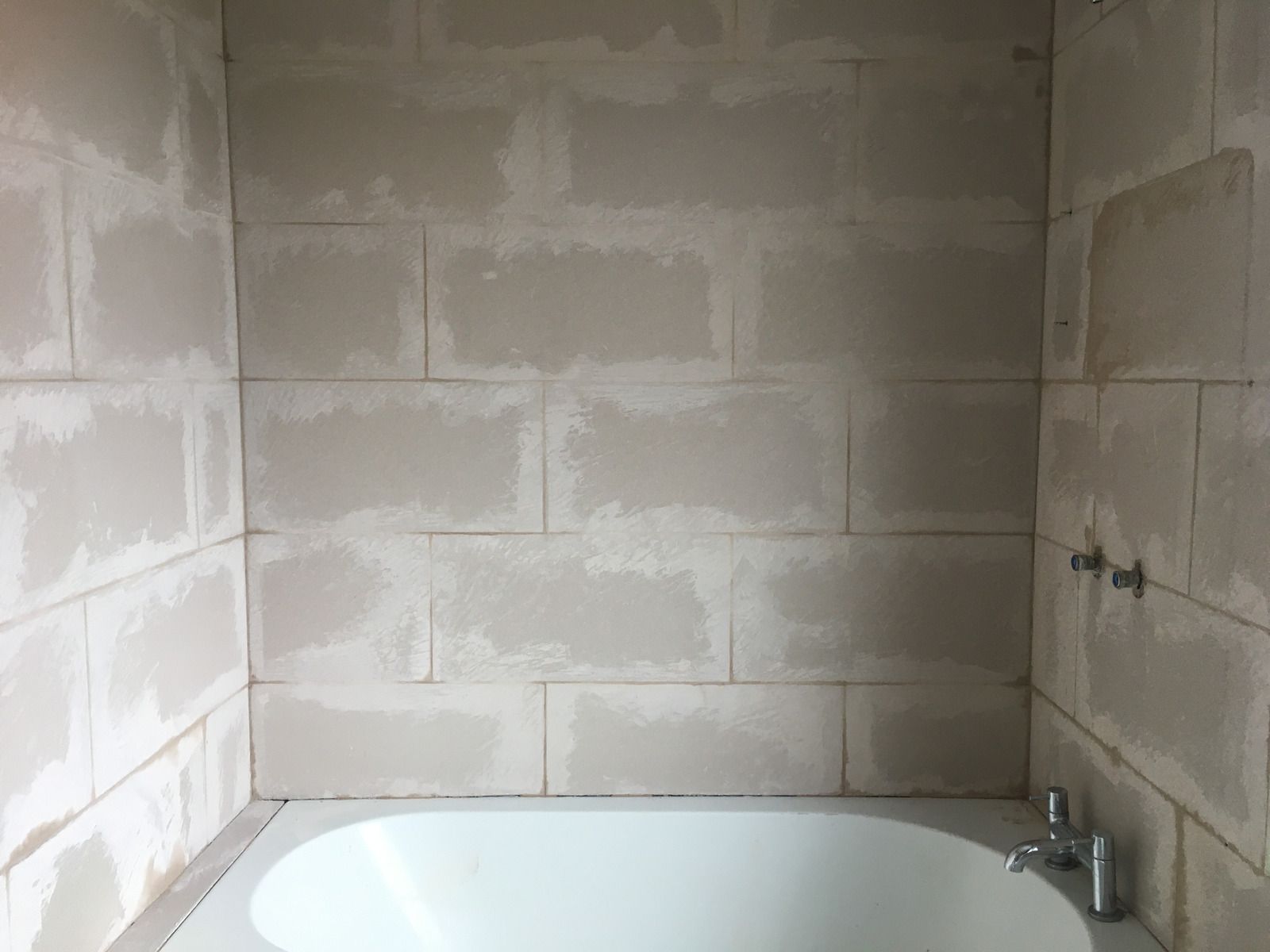 Person in work glove uses a trowel to apply grout between gray tiles.