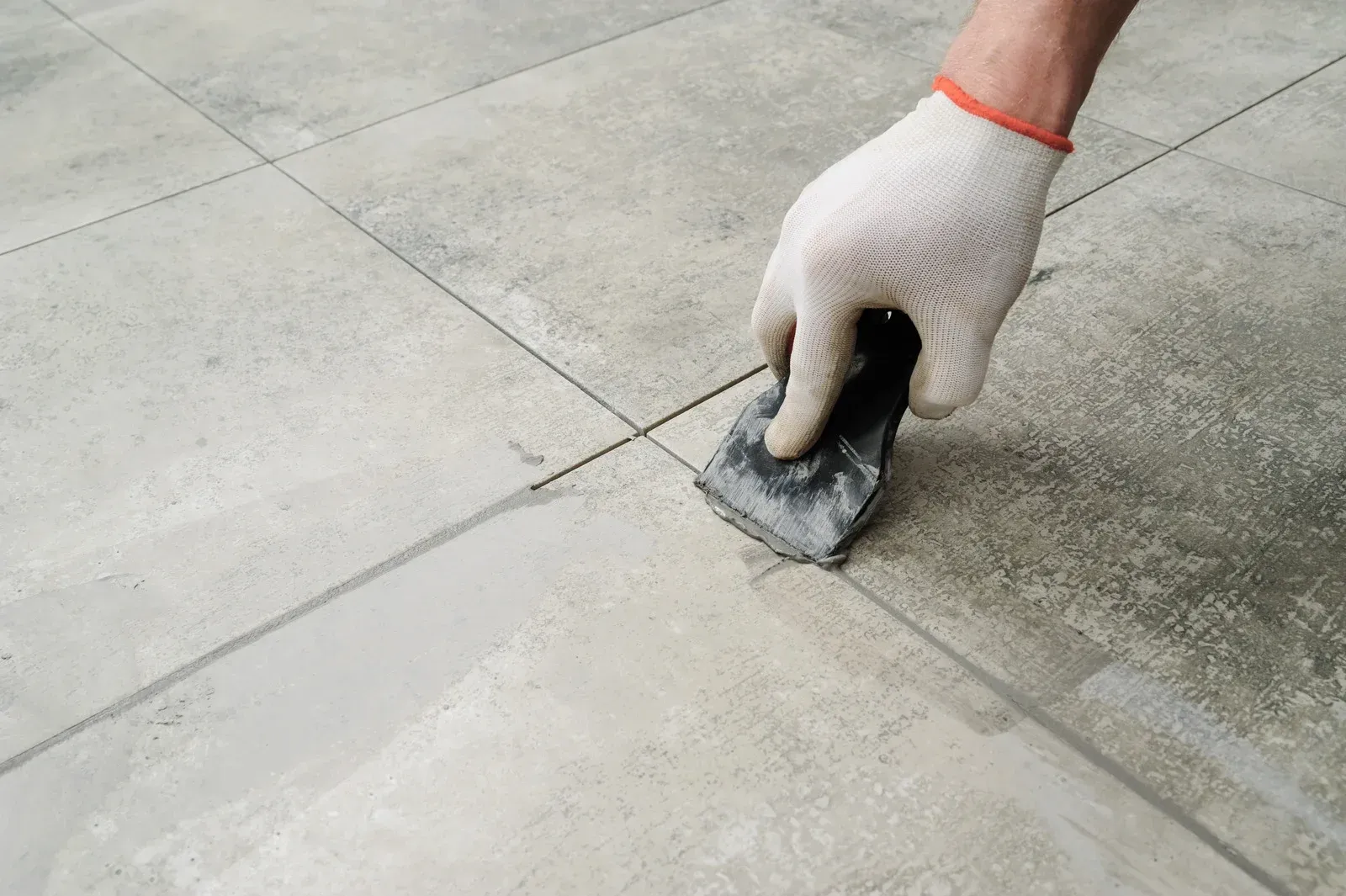 A person is applying grout to a tile floor with a spatula.