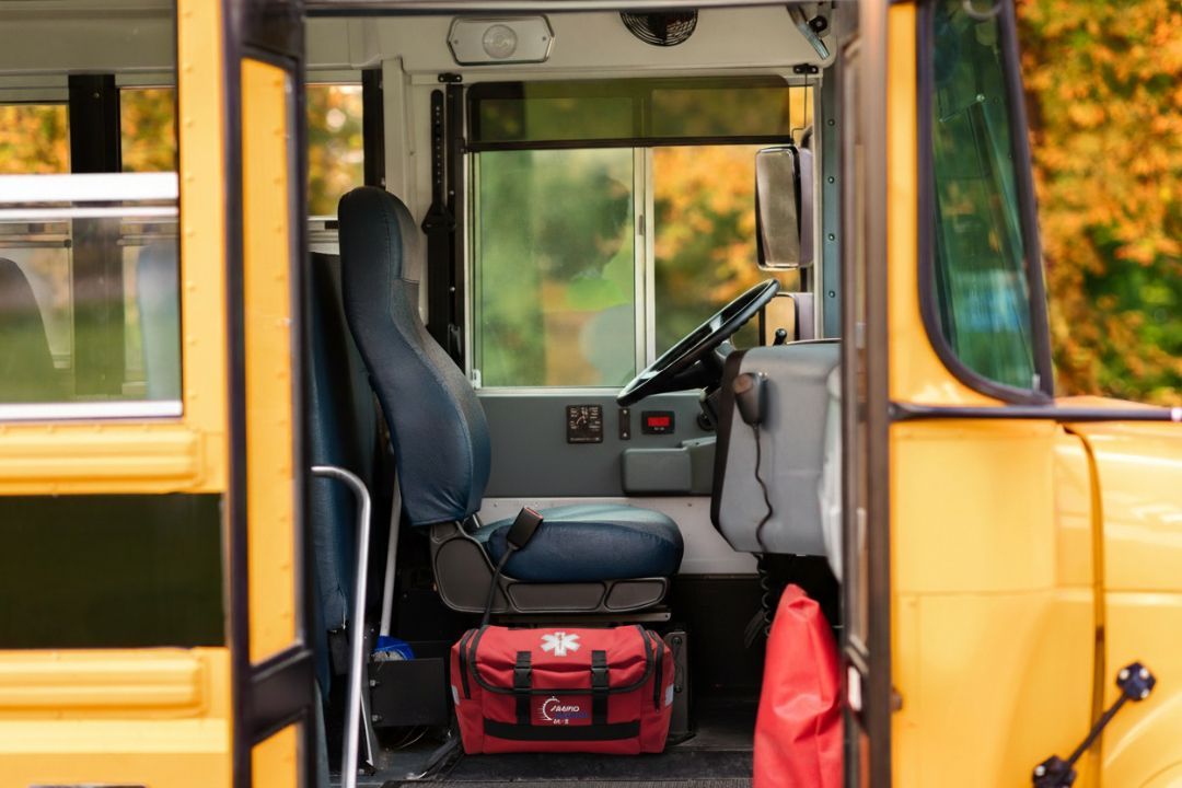 Inside of a yellow school bus, driver's seat with emergency bag and red bag at the bottom.