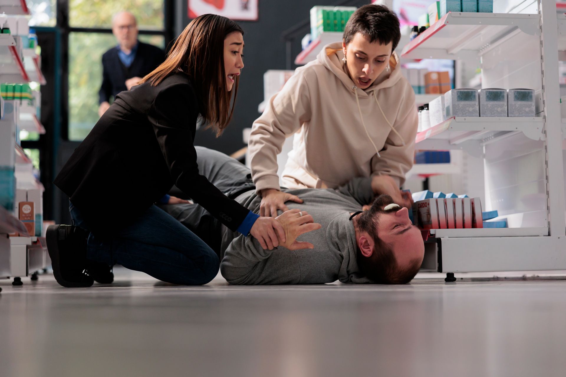 A group of people are helping a man who is laying on the floor in a pharmacy.