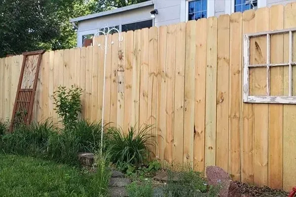 A wooden fence with a window in the backyard of a house.