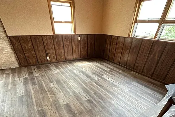 An empty room with wood paneling and hardwood floors.