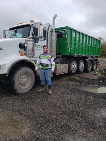 Man in Buzz Lightyear costume stands next to green dump truck on gravel.