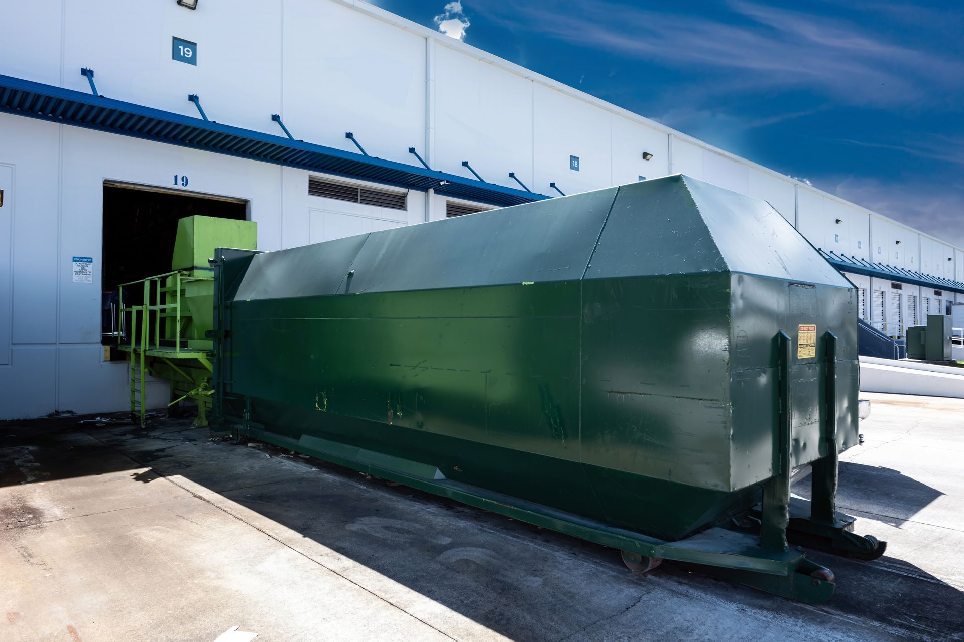 Green industrial waste compactor outside a loading dock.