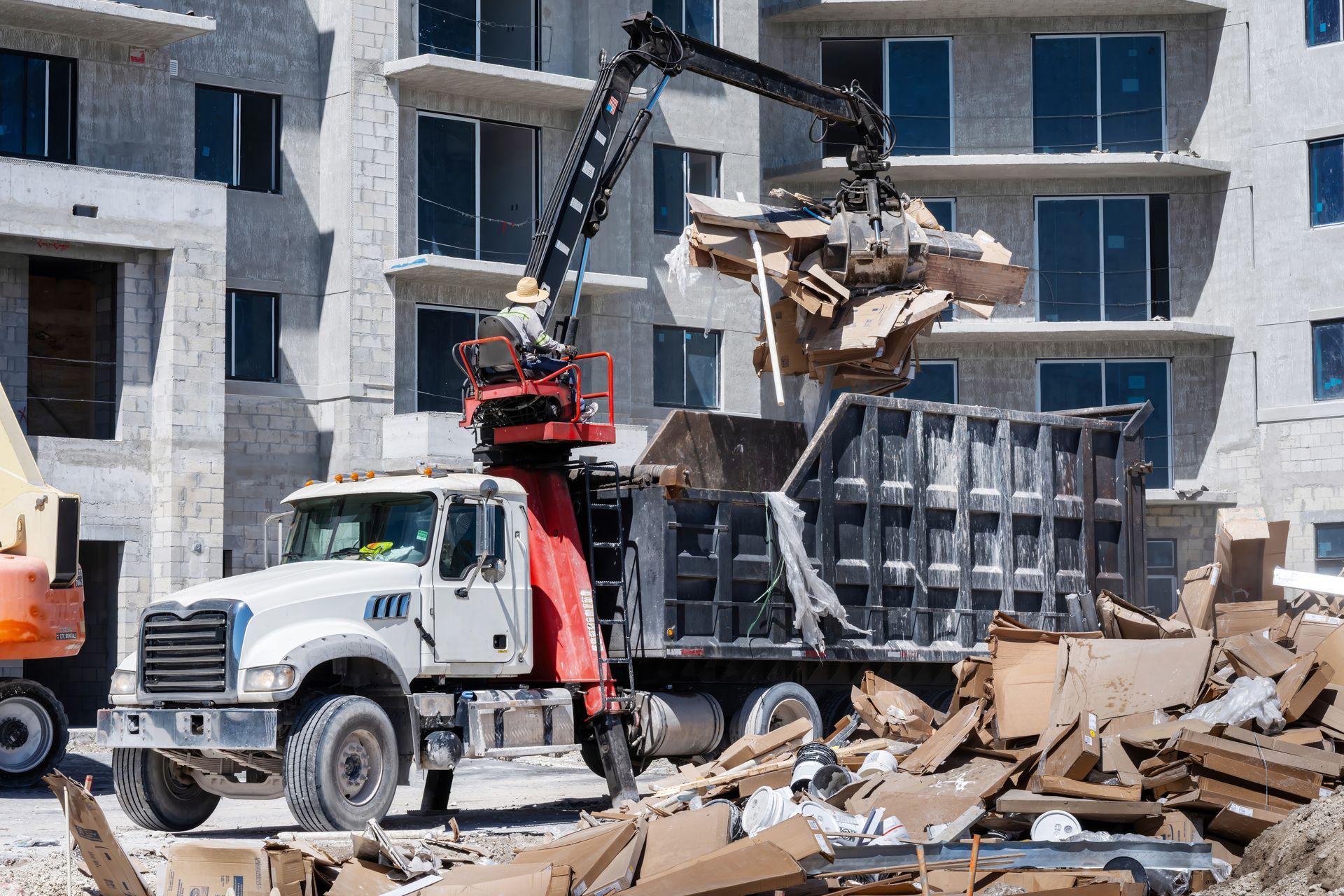 A construction truck loading debris from a building site with a mechanical arm.