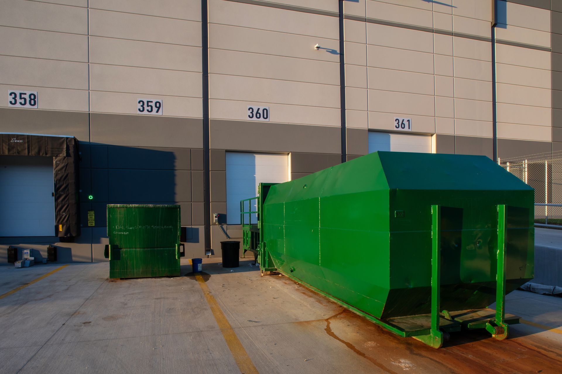 Orange industrial garbage bins, street setting, a green bin, and buildings in the background.