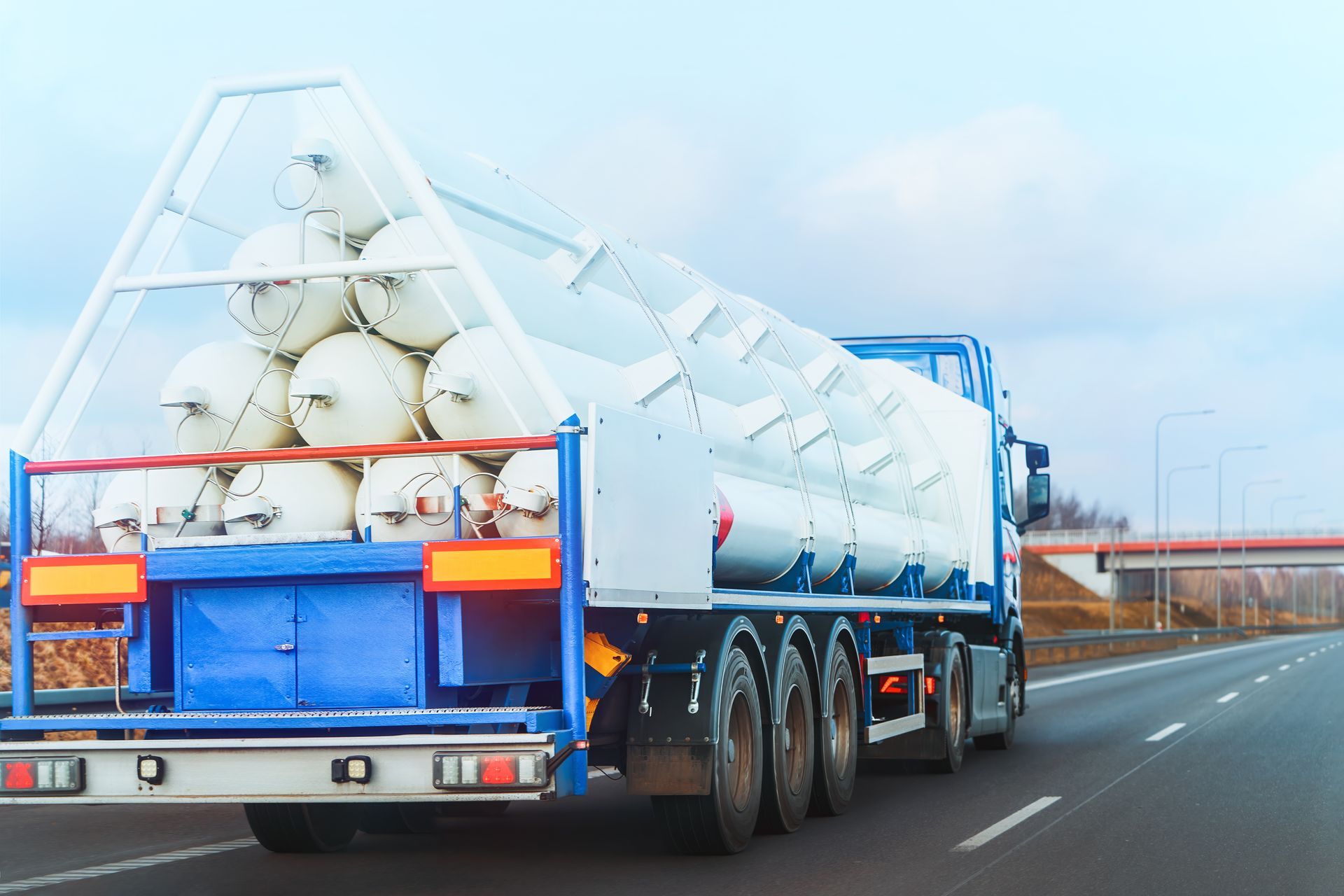 Tanker truck carrying multiple white gas cylinders on highway.