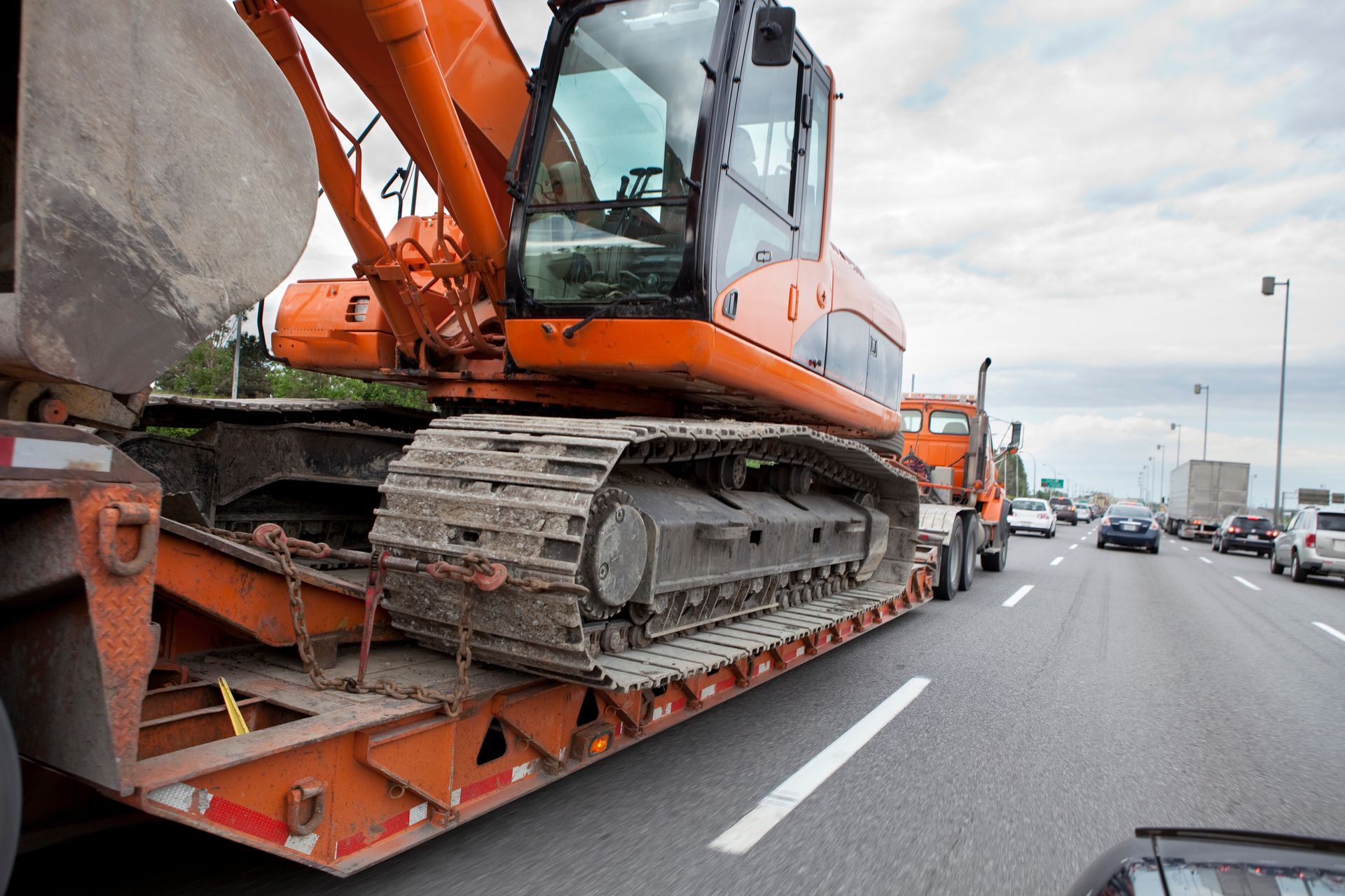 Orange excavator on a flatbed trailer traveling on a highway with other vehicles.