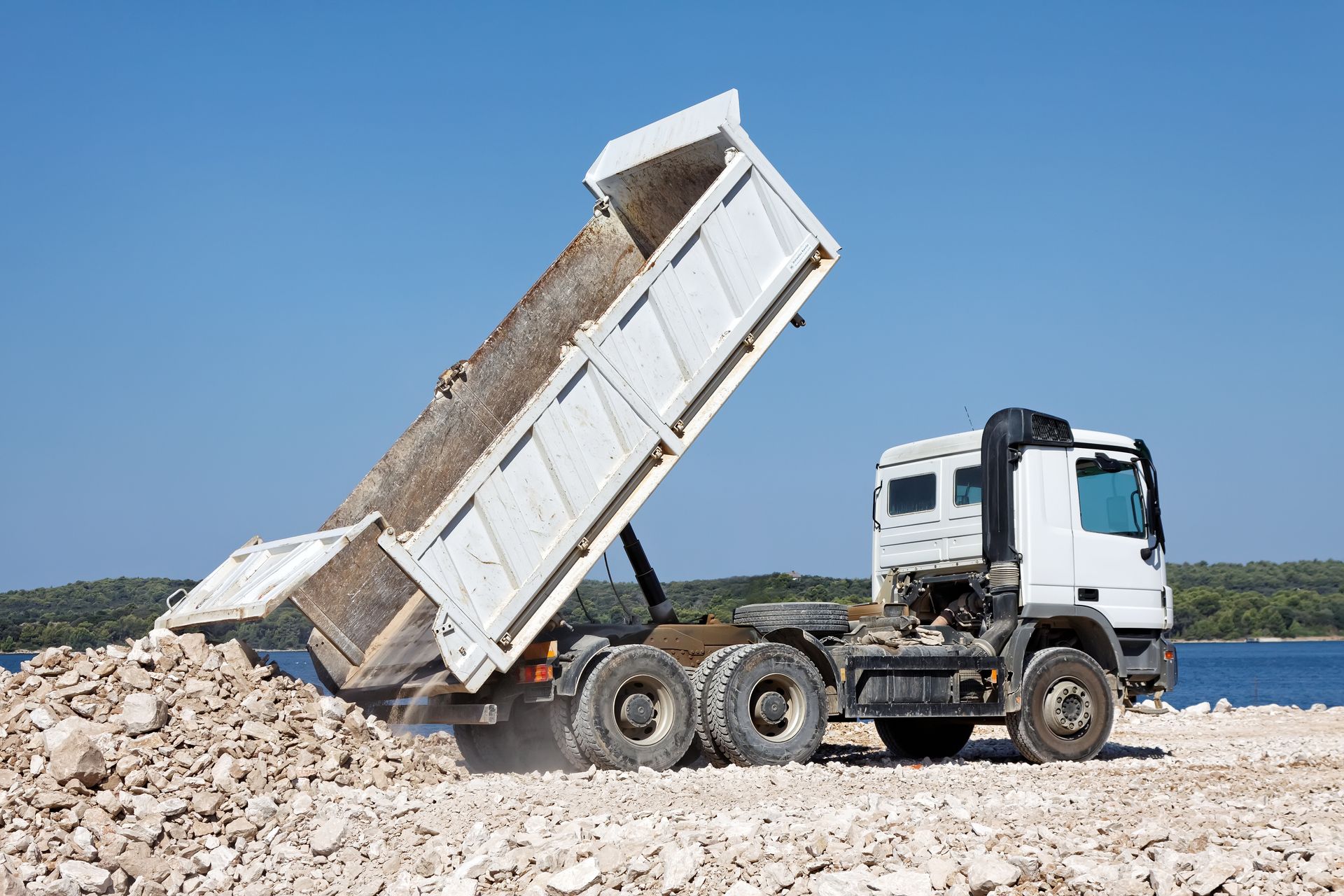 Green dumpster being lifted by a truck in a residential area, containing trash.